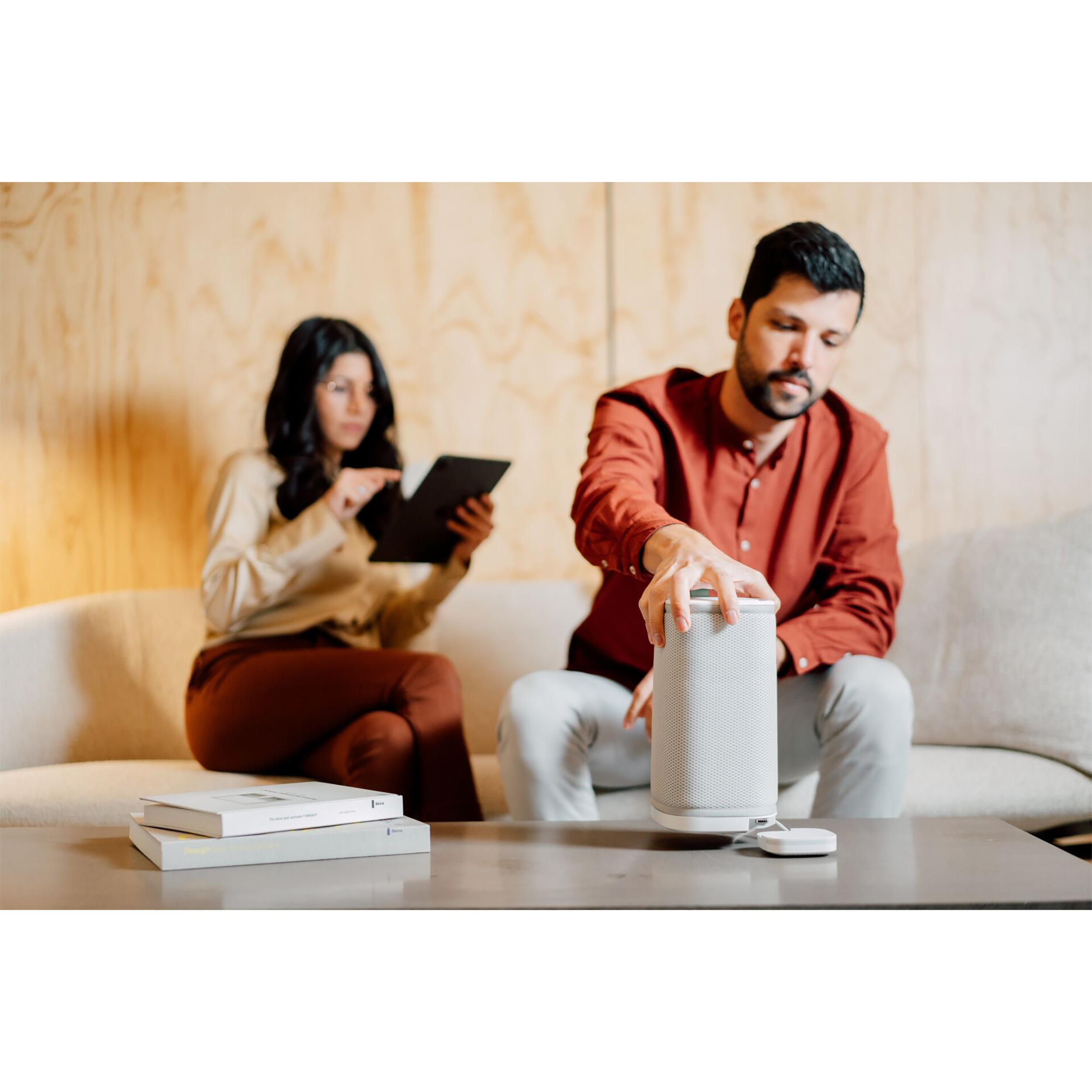 Zwei Personen sitzen auf einer Couch. Einer hält ein Tablet, der andere bedient einen Lautsprecher.