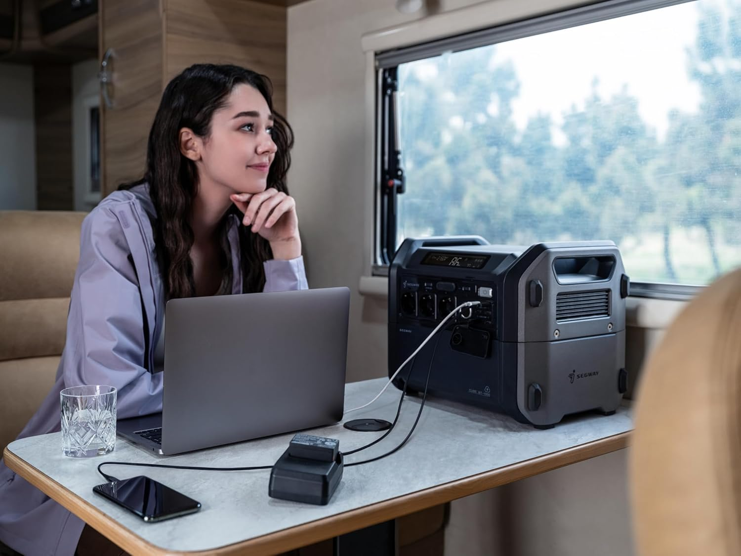 Una mujer usa una laptop en una autocaravana. Una estación de energía y otros accesorios están cerca.