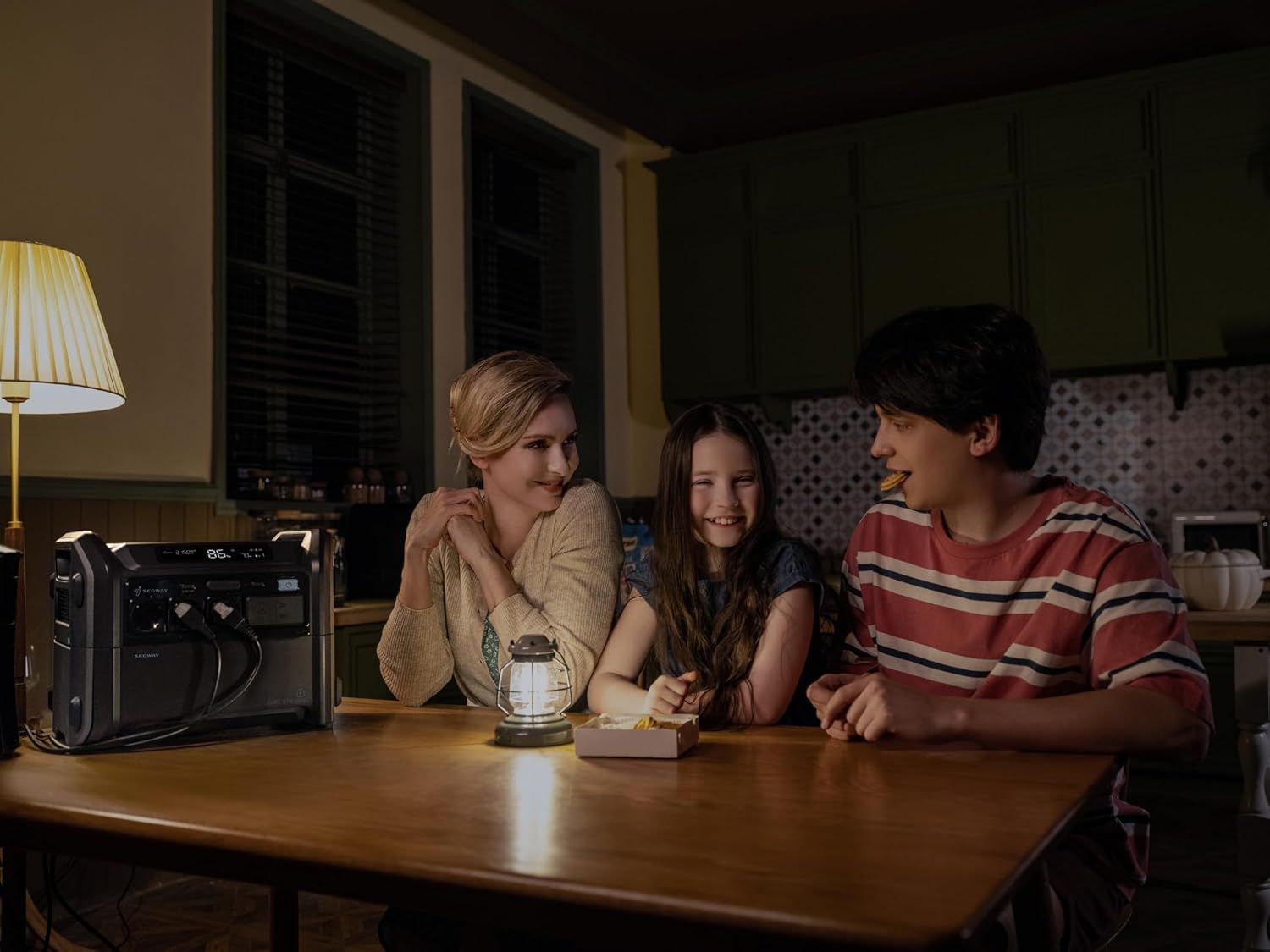 Familia en una habitación con poca luz con una estación de energía portátil. Mesa, linterna, bocadillos.
