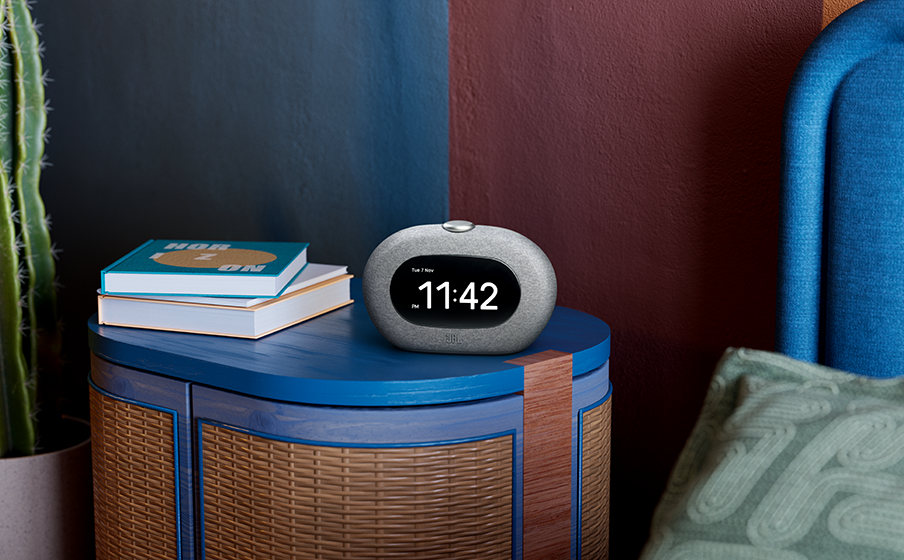 Radio-réveil JBL Horizon 3 affichant 11h42, sur un meuble bleu, avec des livres et un oreiller.