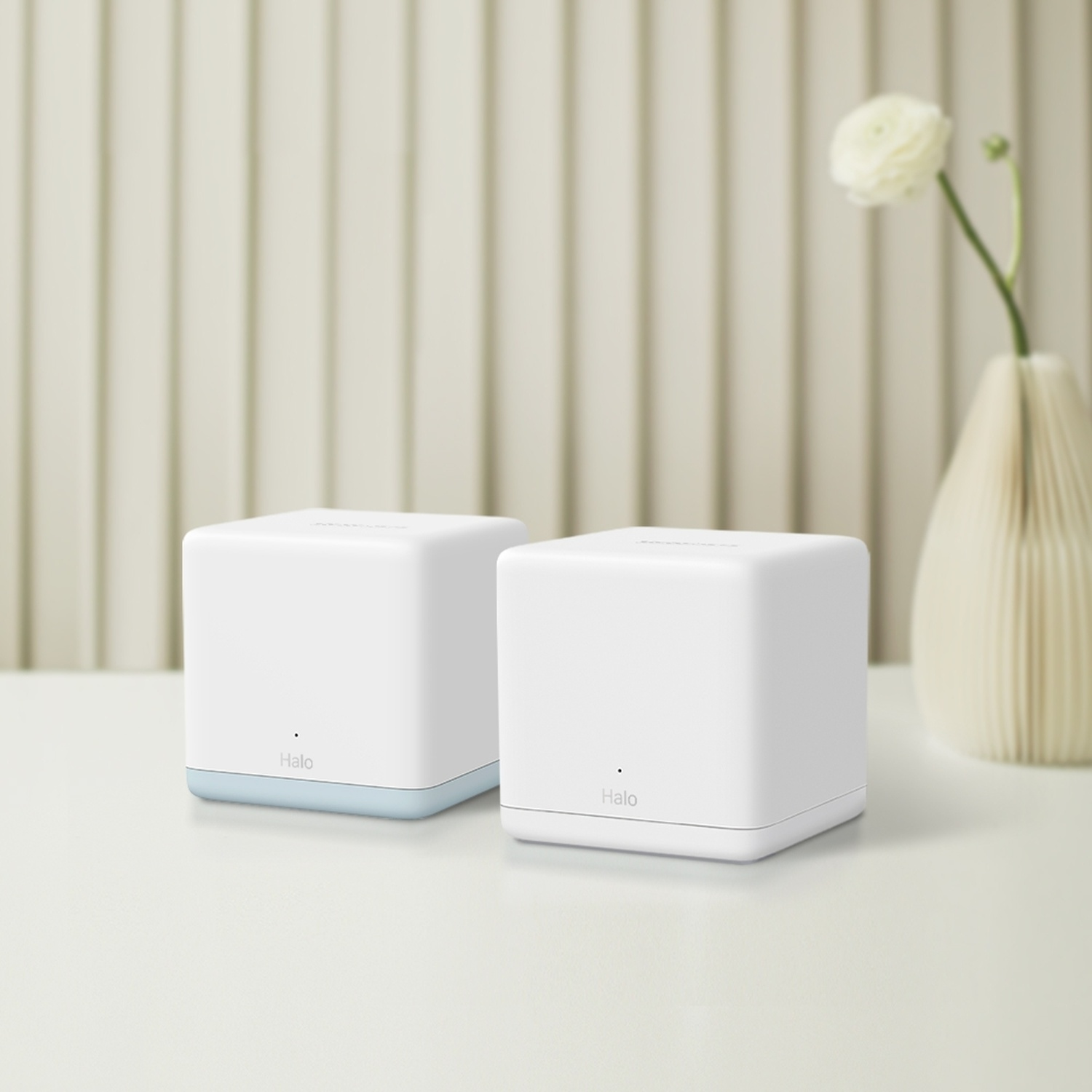 Due unità mesh Wi-Fi bianche su un tavolo, con un vaso e un fiore sullo sfondo.