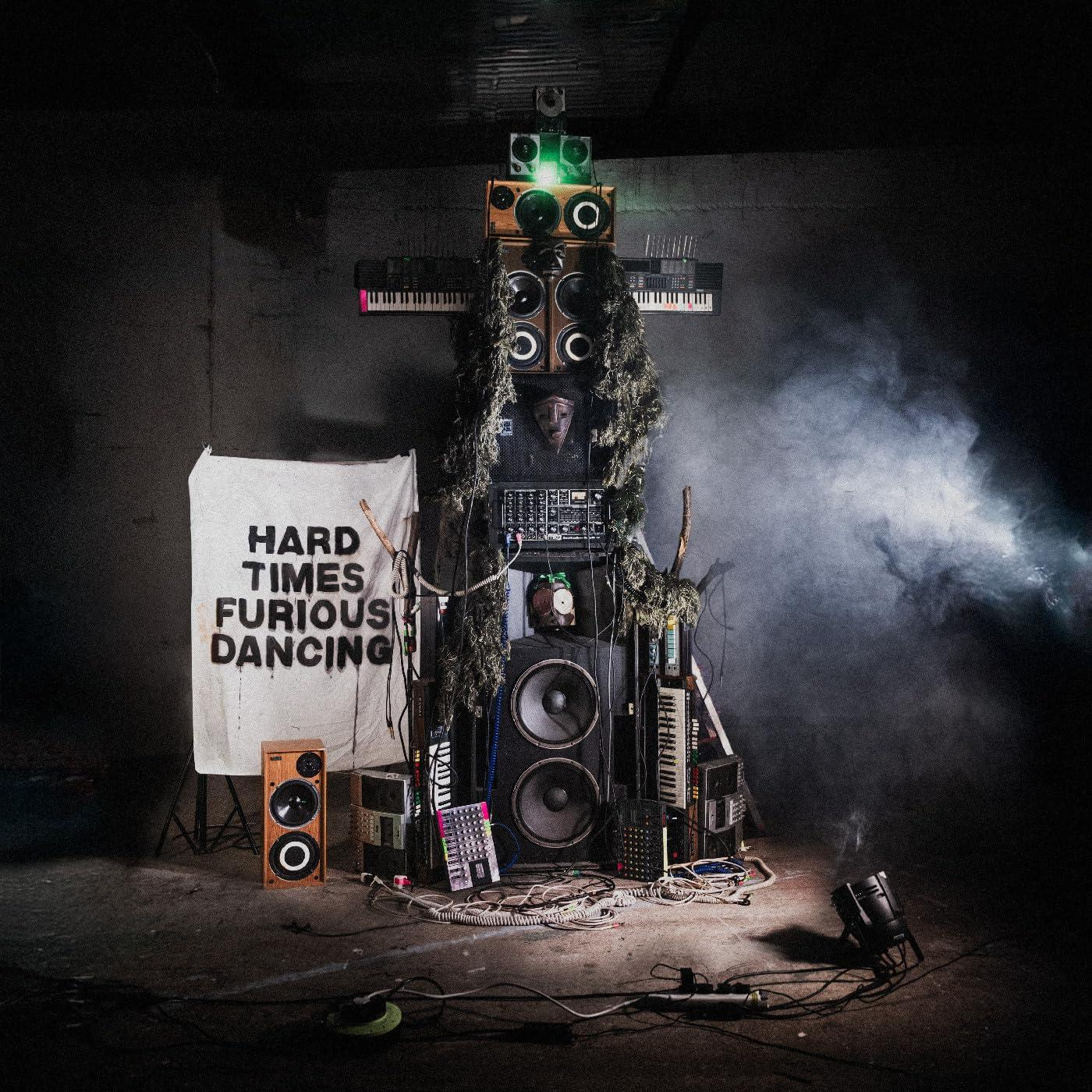 Ein komplexes Setup aus Lautsprechern, Instrumenten und einem Banner mit der Aufschrift 'HARD TIMES...DANCING'.