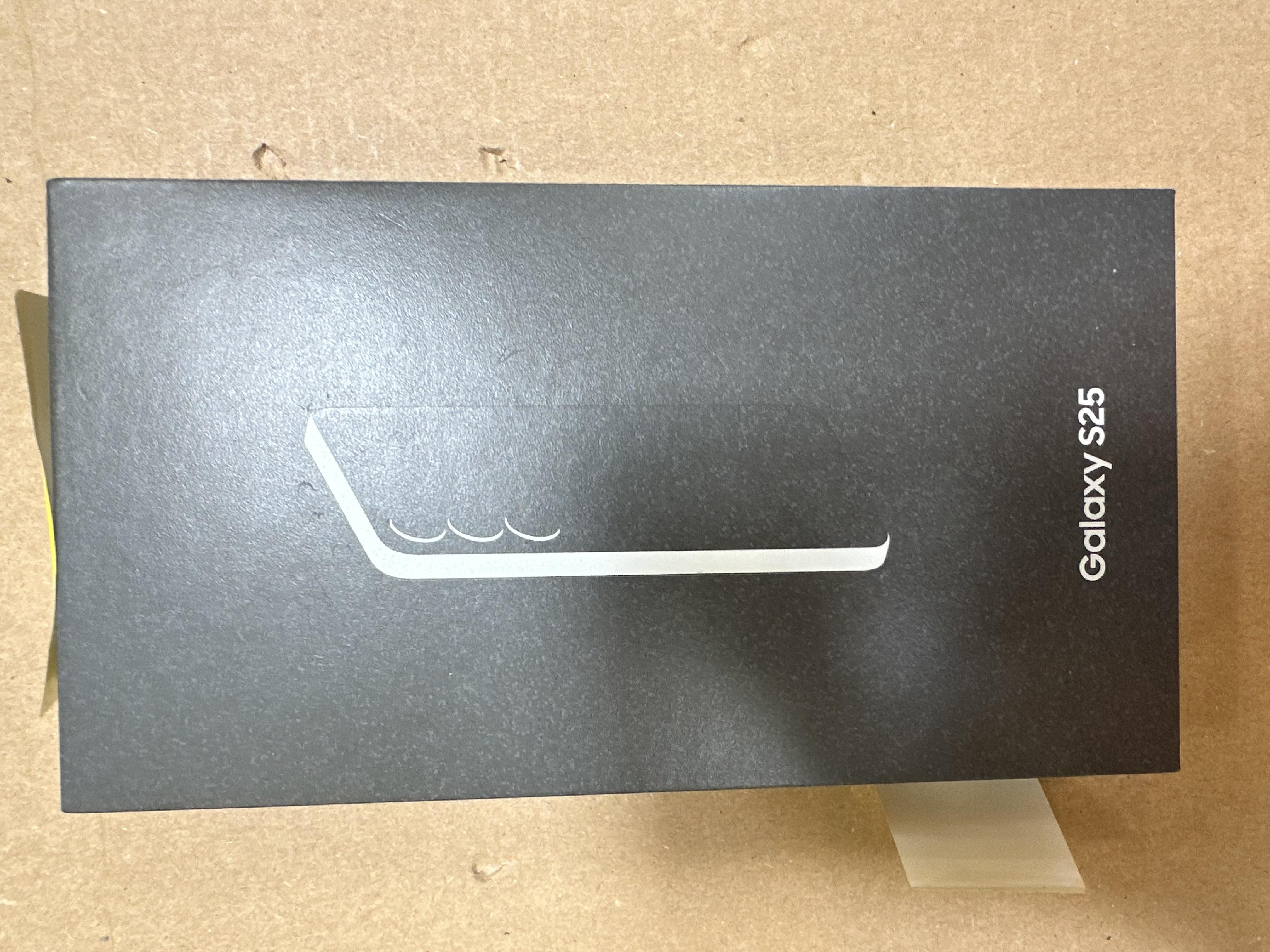 Czarne pudełko. Na górze biały zarys telefonu. Tekst z boku mówi Galaxy S25.