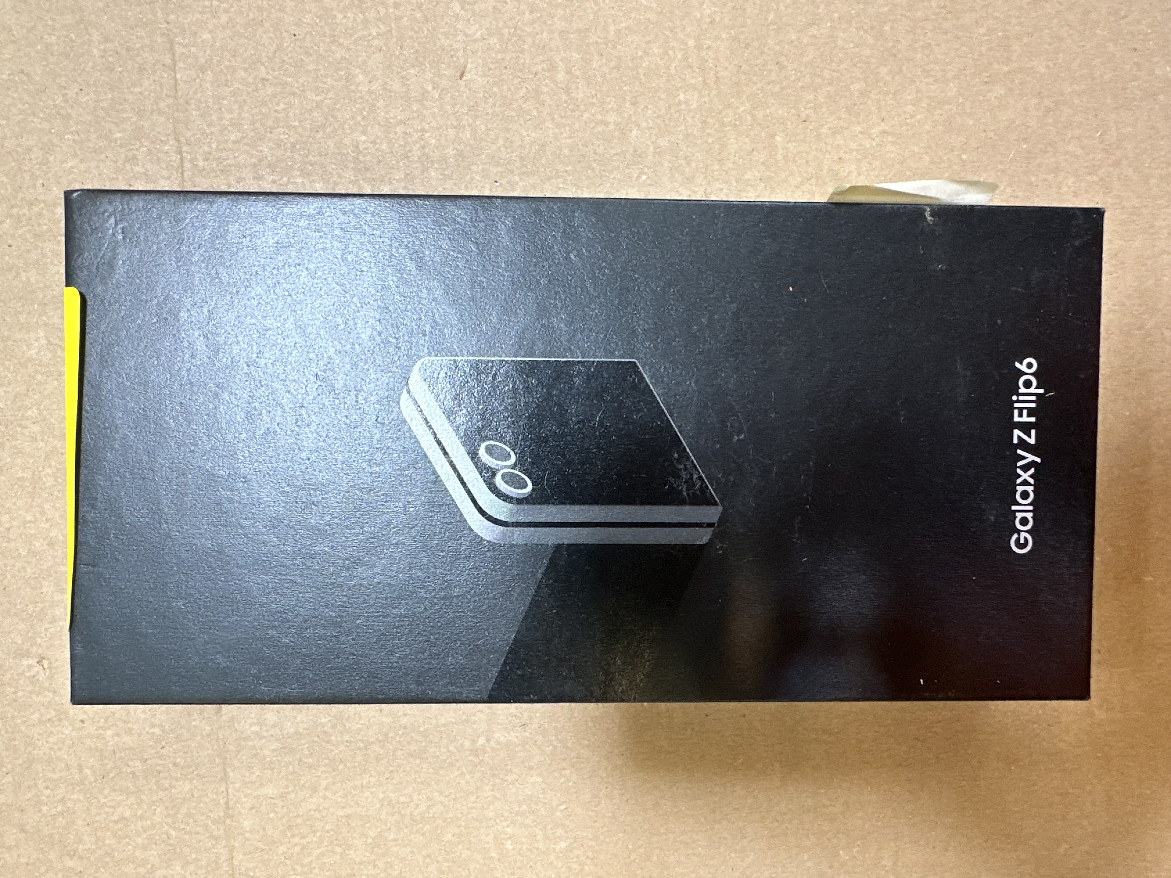 Czarne pudełko na telefon z zamkniętym telefonem w środku. Pudełko ma napis Galaxy Z Flip6.