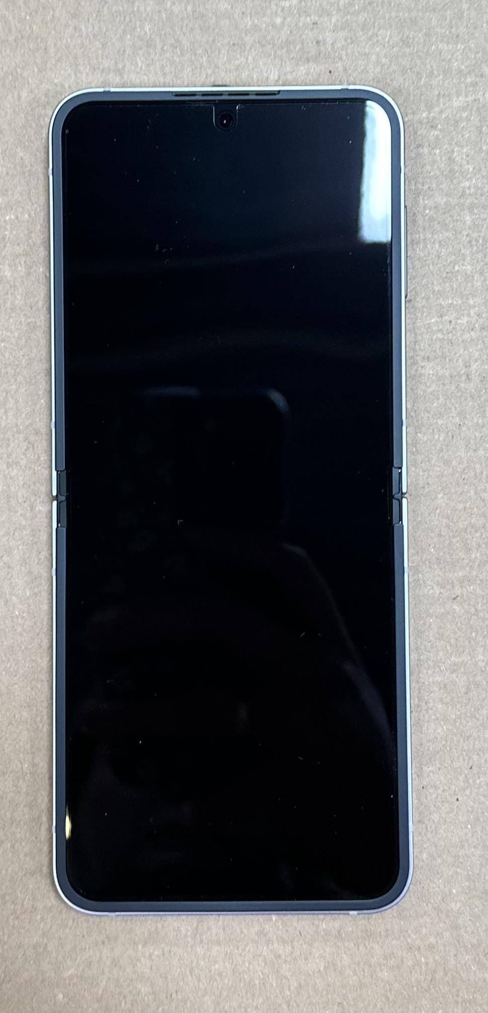 Czarny telefon, rozłożony, na kartonowej powierzchni. Ekran widoczny, ramka srebrna.