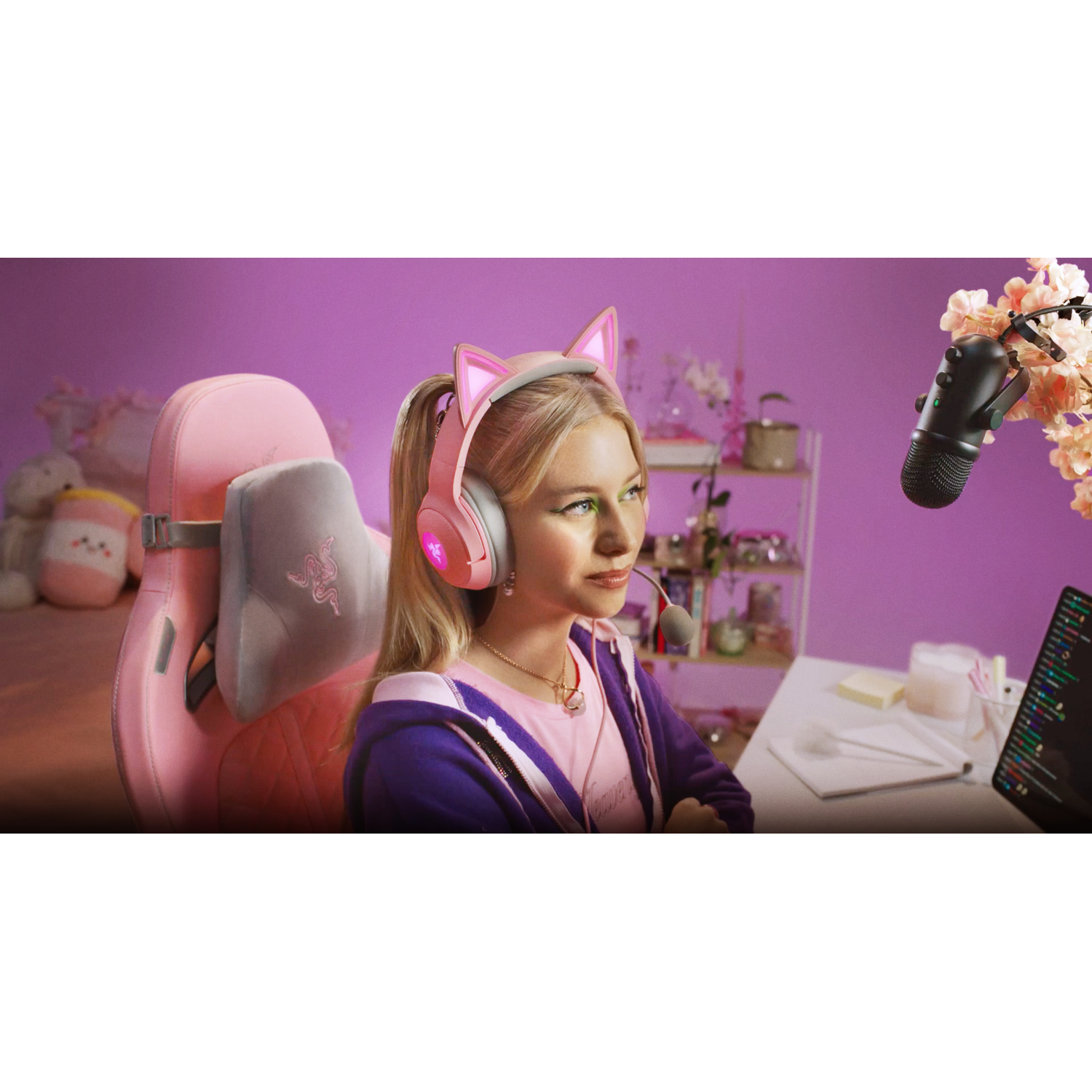 Blonde woman with a pink headset, sitting in a gaming chair, streaming, and smiling.