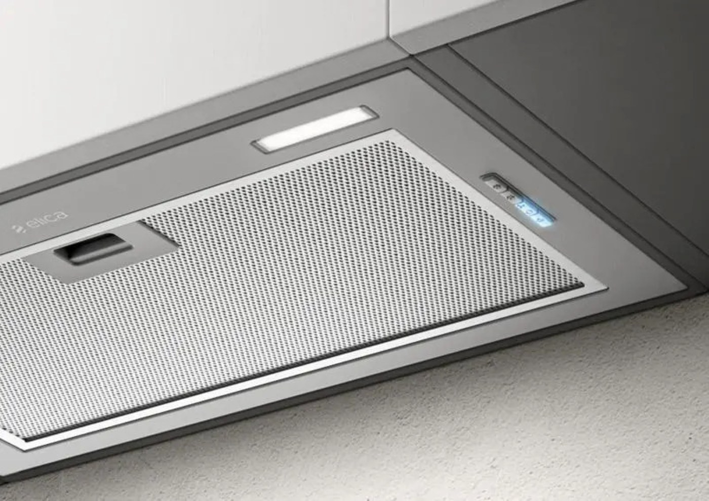 Zbliżenie na okap. Ma metalowy filtr siatkowy i światła.