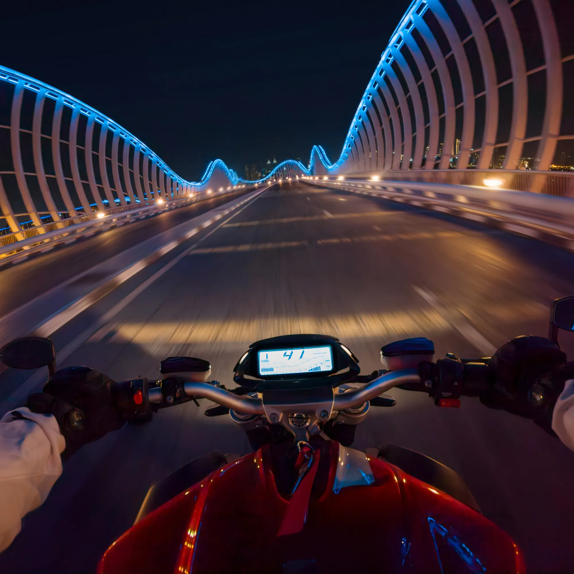 Motorrad fährt nachts auf einer Brücke mit blauen Lichtern. Der Fahrer steht im Fokus.