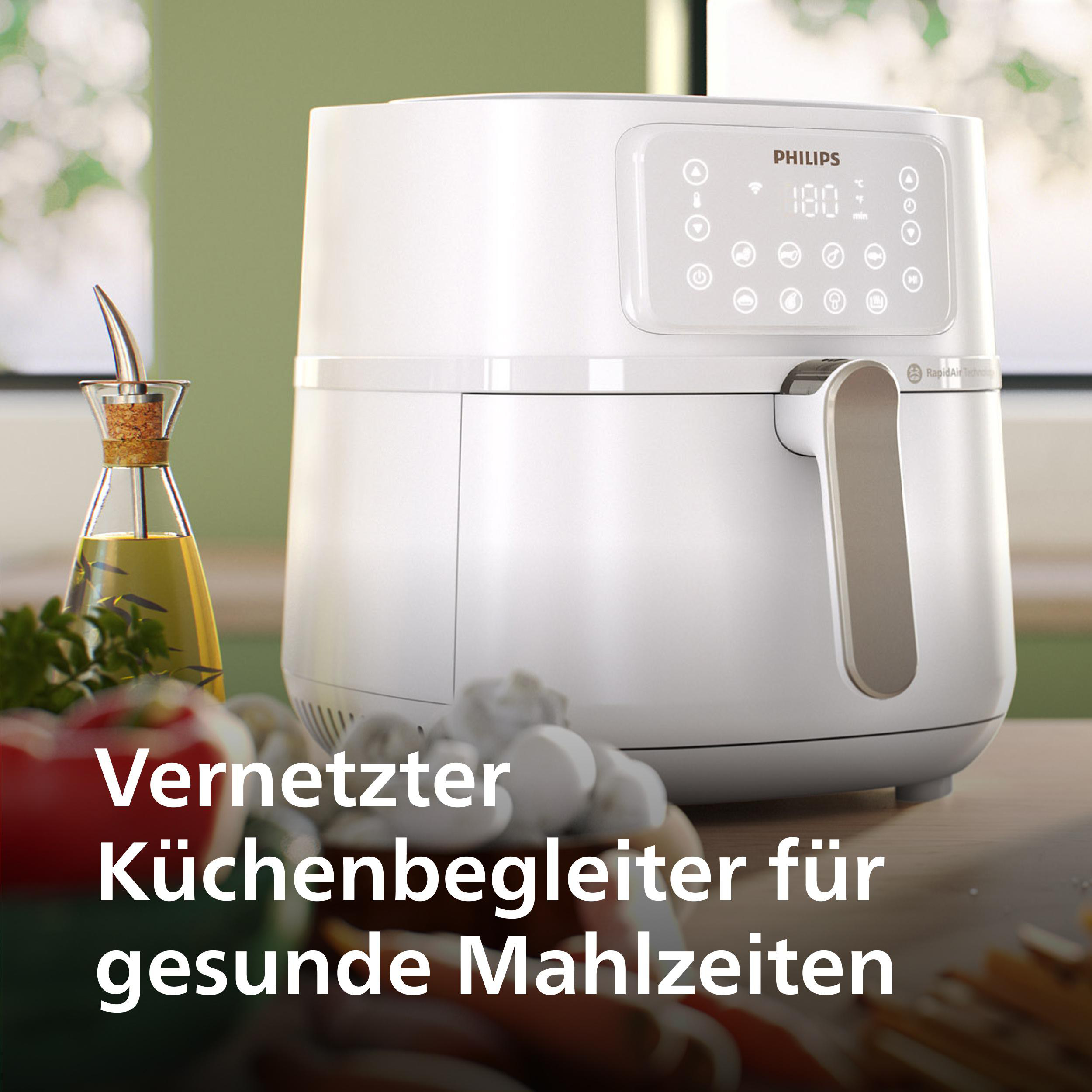 Weißer Heißluftfritteuse auf einer Küchentheke mit Gemüse und Öl. Grüner Hintergrund.