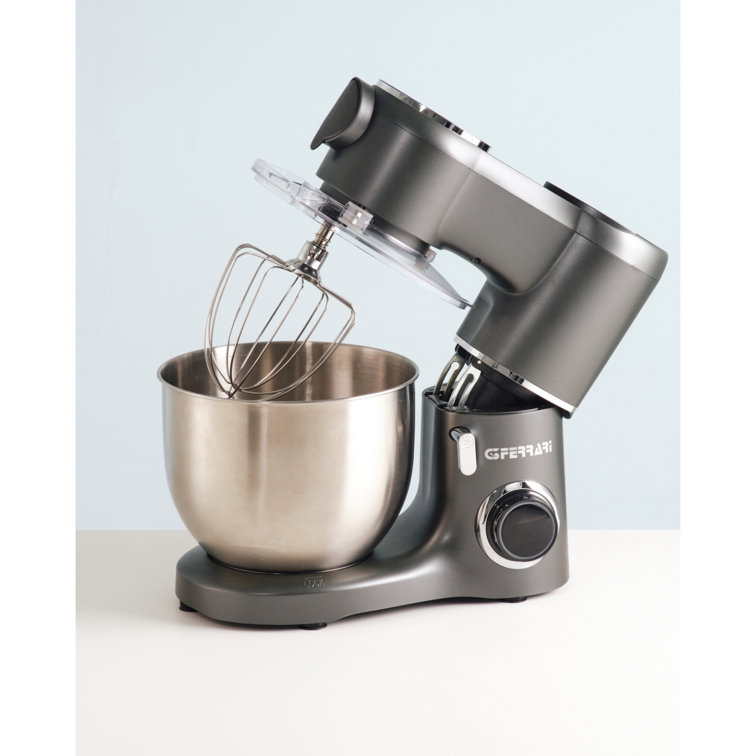 Mixer planetario grigio con frusta e ciotola, su superficie bianca contro sfondo blu.