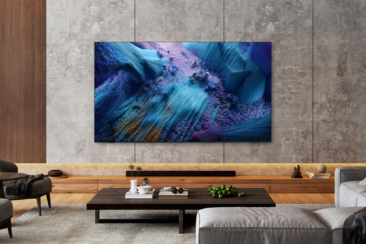 TV montata a parete, con arte astratta. Tavolino e divano di fronte.