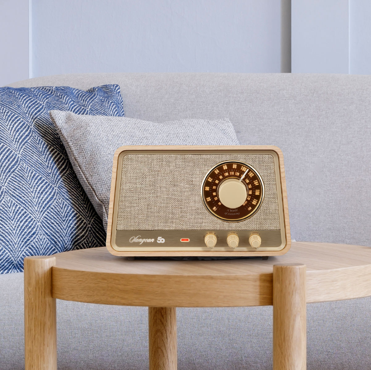 Holzradio auf einem Tisch. Sofa und Kissen im Hintergrund. Weißer Hintergrund.