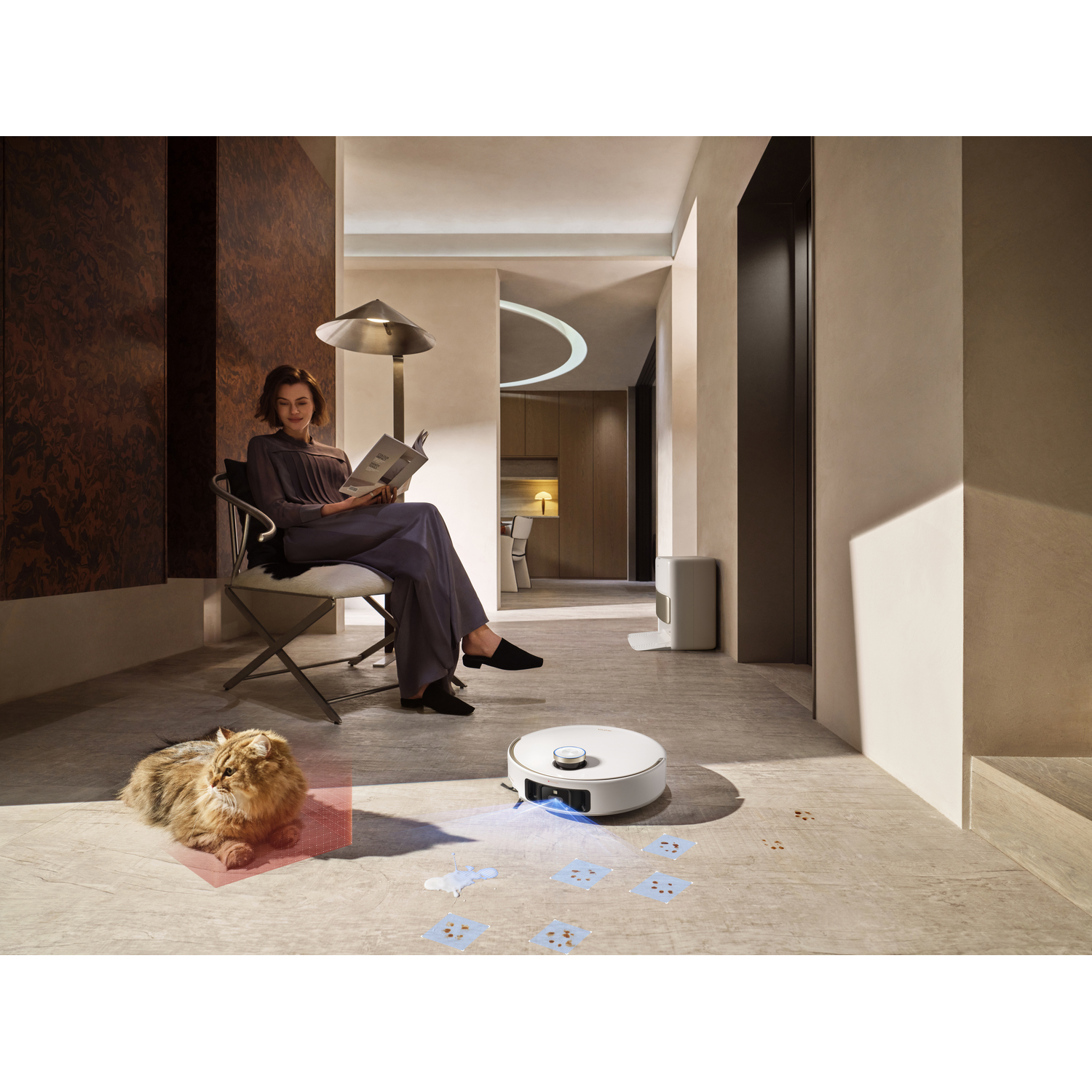 Woman reading, cat nearby, robot vacuum cleaning. Interior scene.