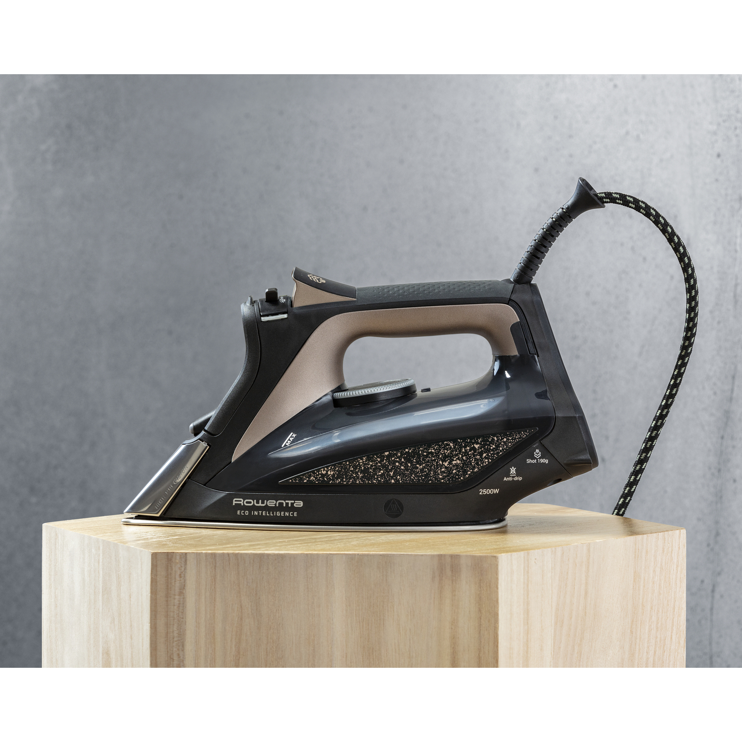 A black iron with gold and tan accents is on a wooden block, against a gray background.