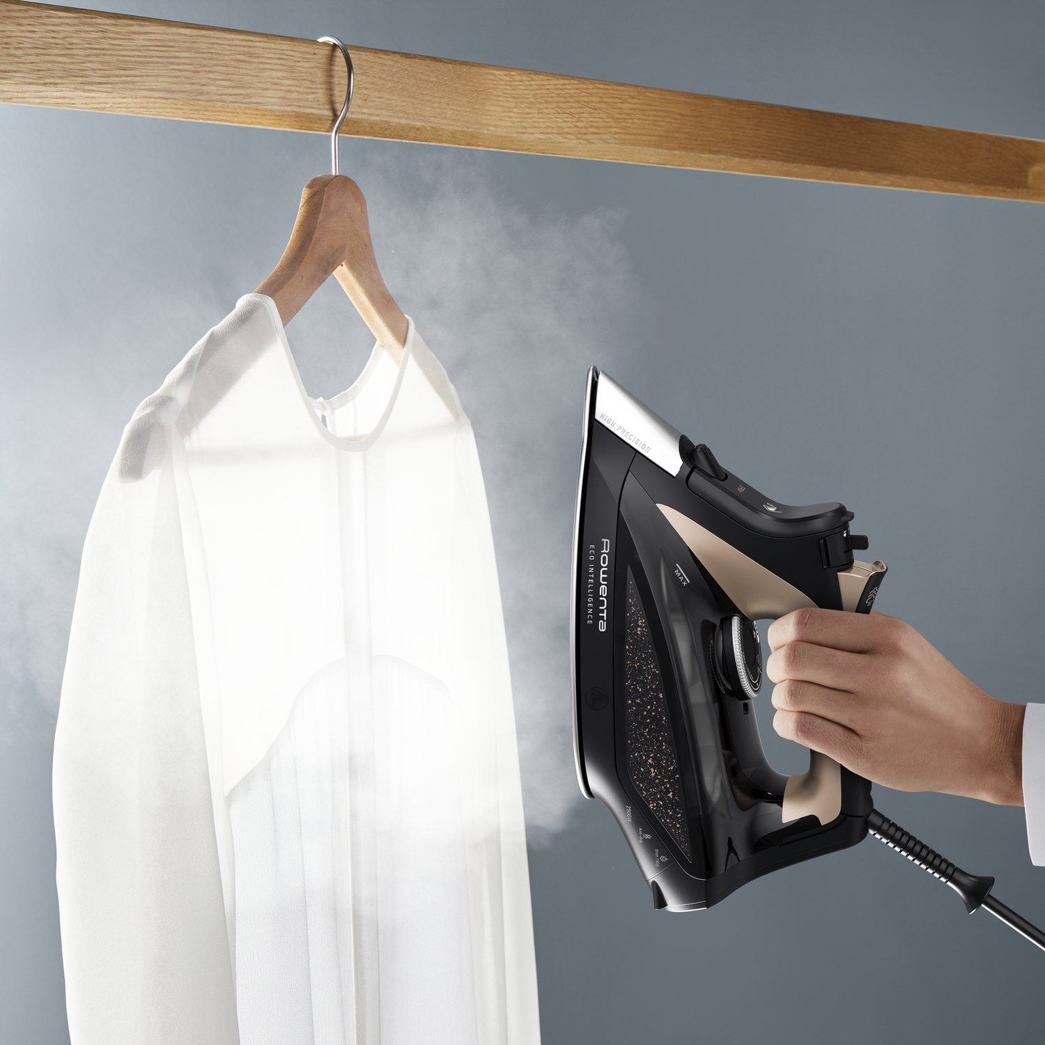A person ironing a white shirt. The iron is black and gold, and the shirt hangs on a wooden hanger.