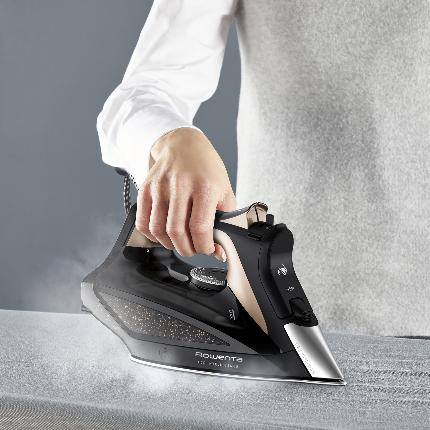 A person ironing on a gray surface. They hold a black and gold iron and steam is coming out.