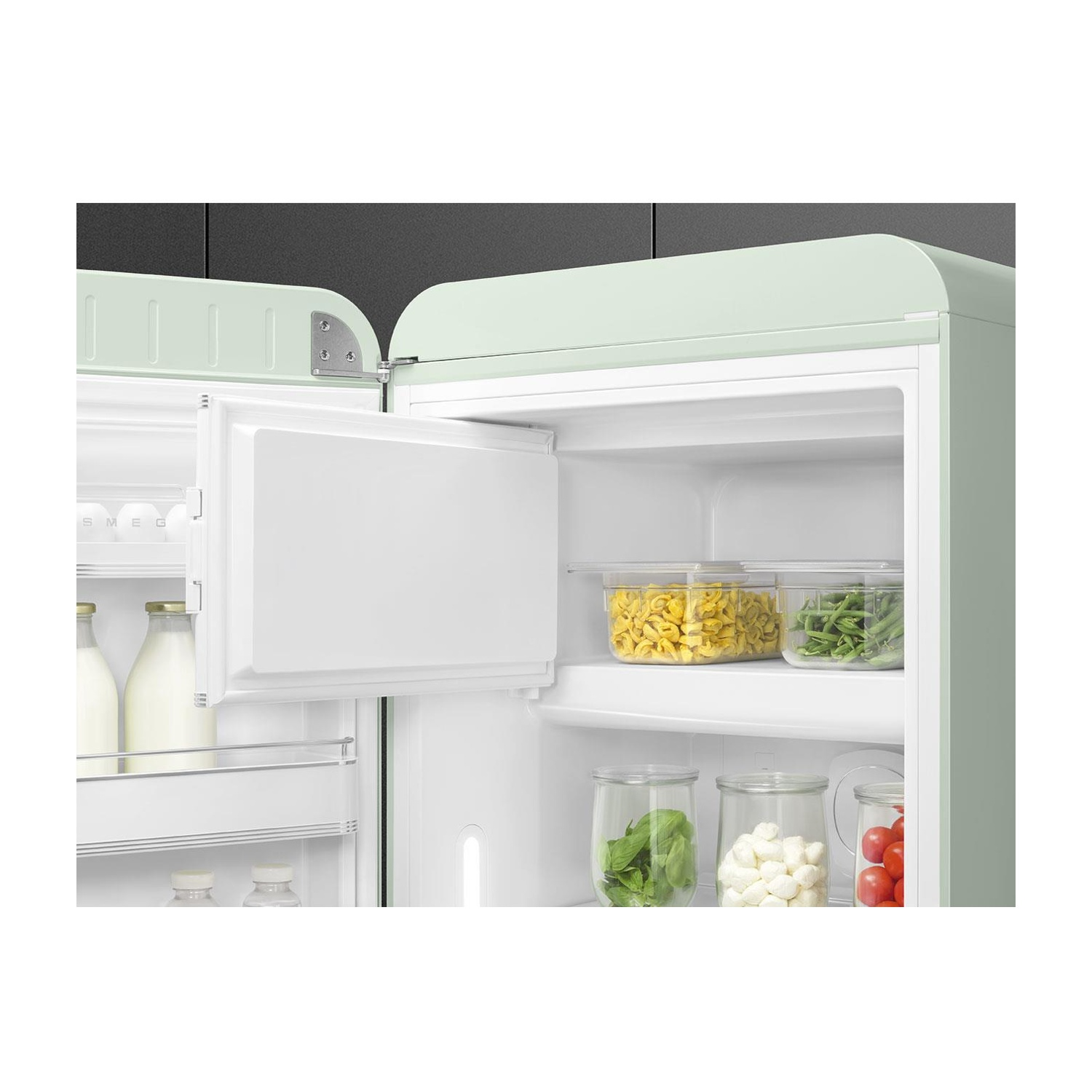 Interno di un frigorifero SMEG verde chiaro. Contiene ripiani con alimenti. Porta del congelatore aperta.