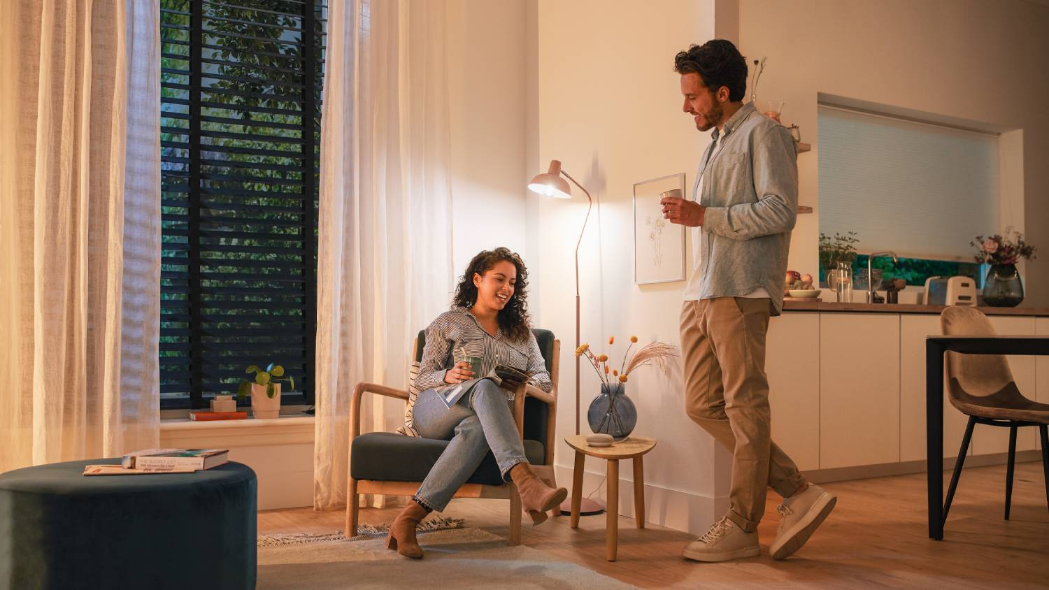 Una pareja en una sala de estar. Están sentados y hablando, con un interior de tonos neutros e iluminación suave.
