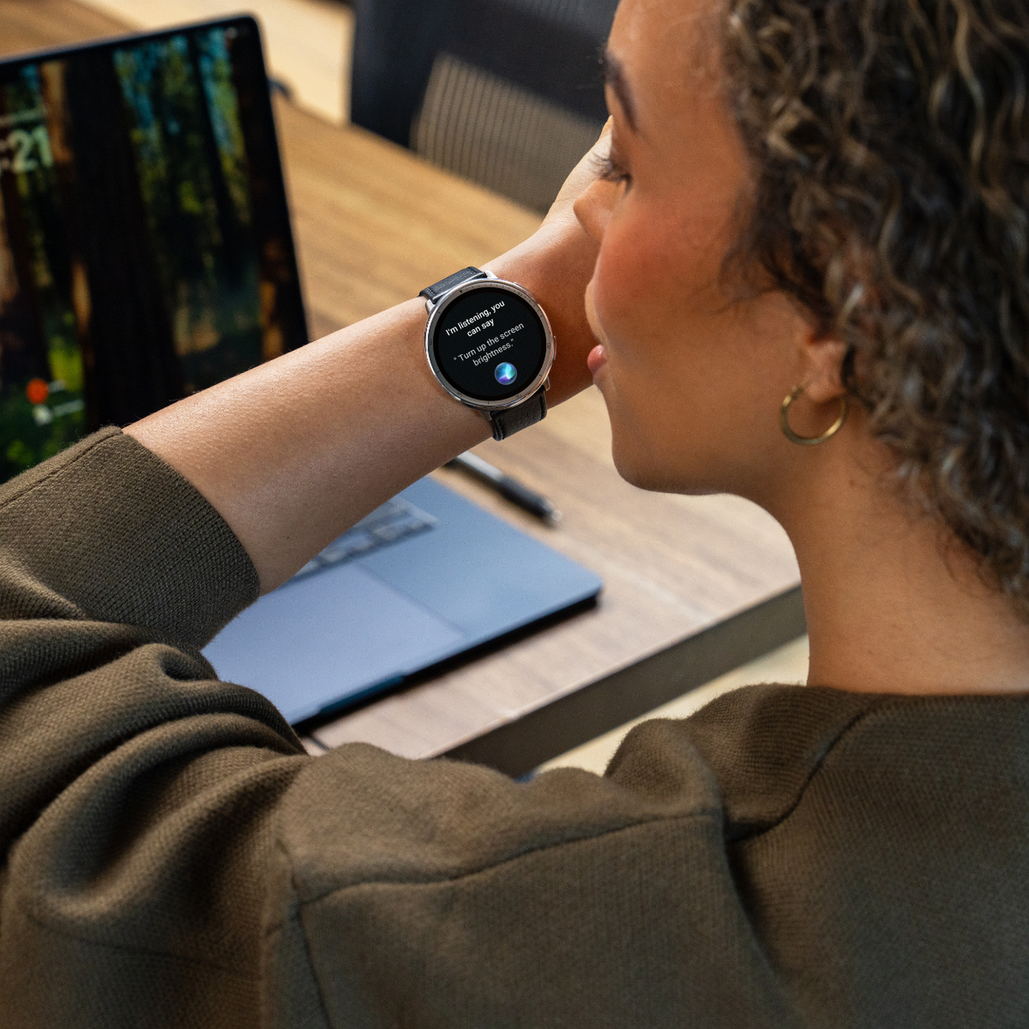Mujer usando un smartwatch con una interfaz de control por voz en un escritorio.