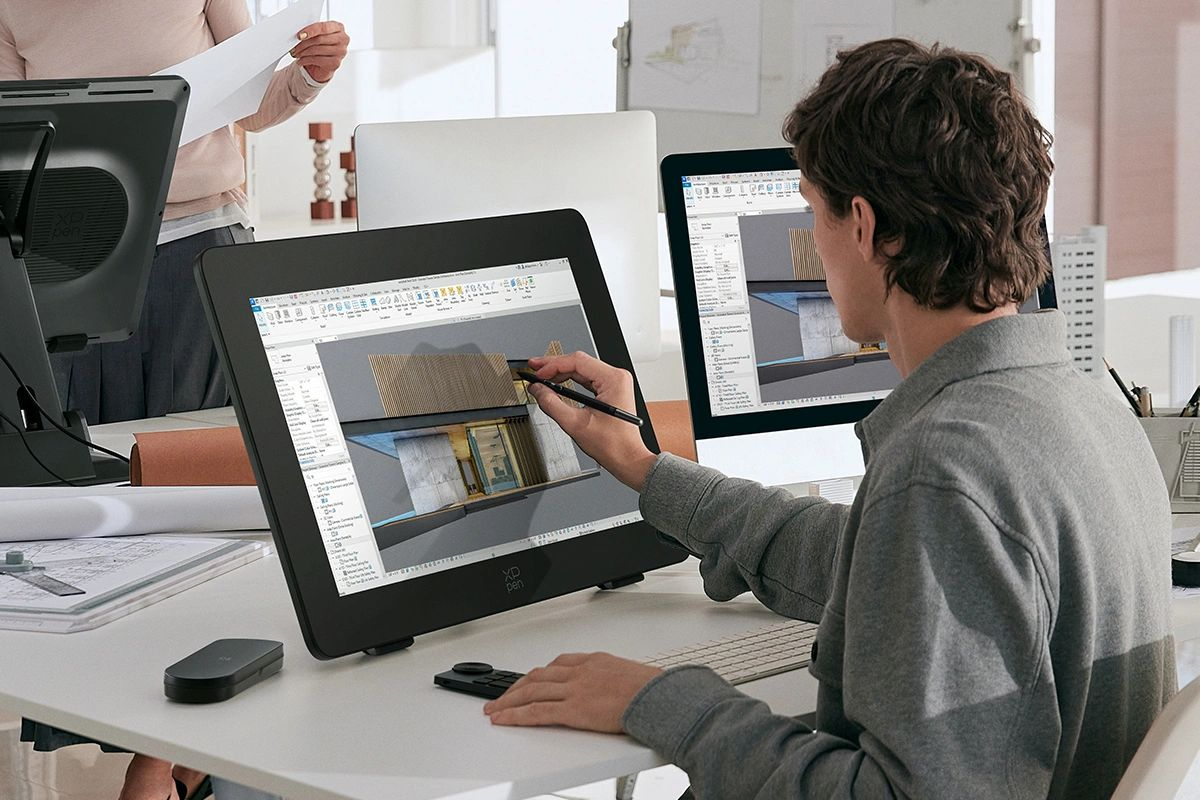 Mann benutzt Stift auf Tablet, zwei Monitore zeigen Design.