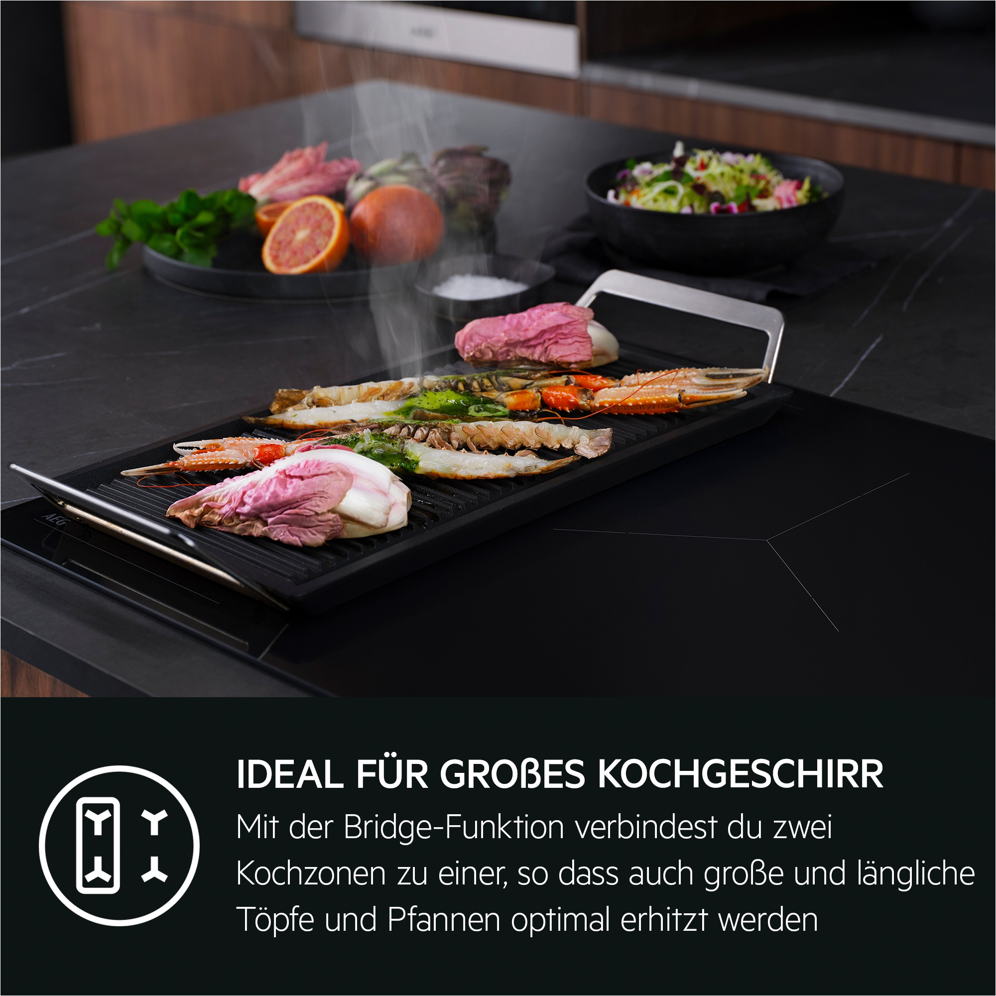 Ein schwarzes Kochfeld mit Essen, darunter Garnelen und Fleisch. Eine schwarze Schüssel mit Salat im Hintergrund.
