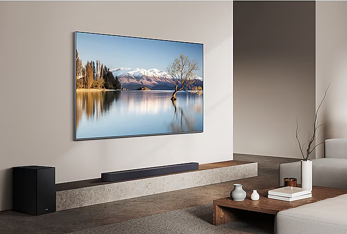Telewizor wyświetlający scenę jeziora, z soundbarem na półce i subwooferem na podłodze.