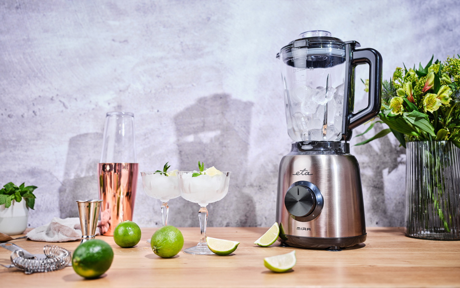 Turmixgép jéggel. Koktélok poharakban, lime-ok és shaker a pulton.