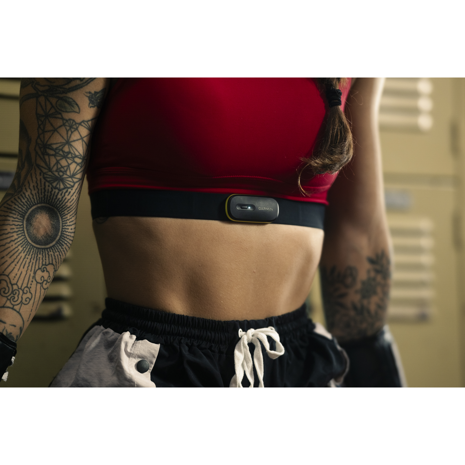 Vrouw draagt rode sport-bh en Garmin hartslagmeter, staat bij lockers.