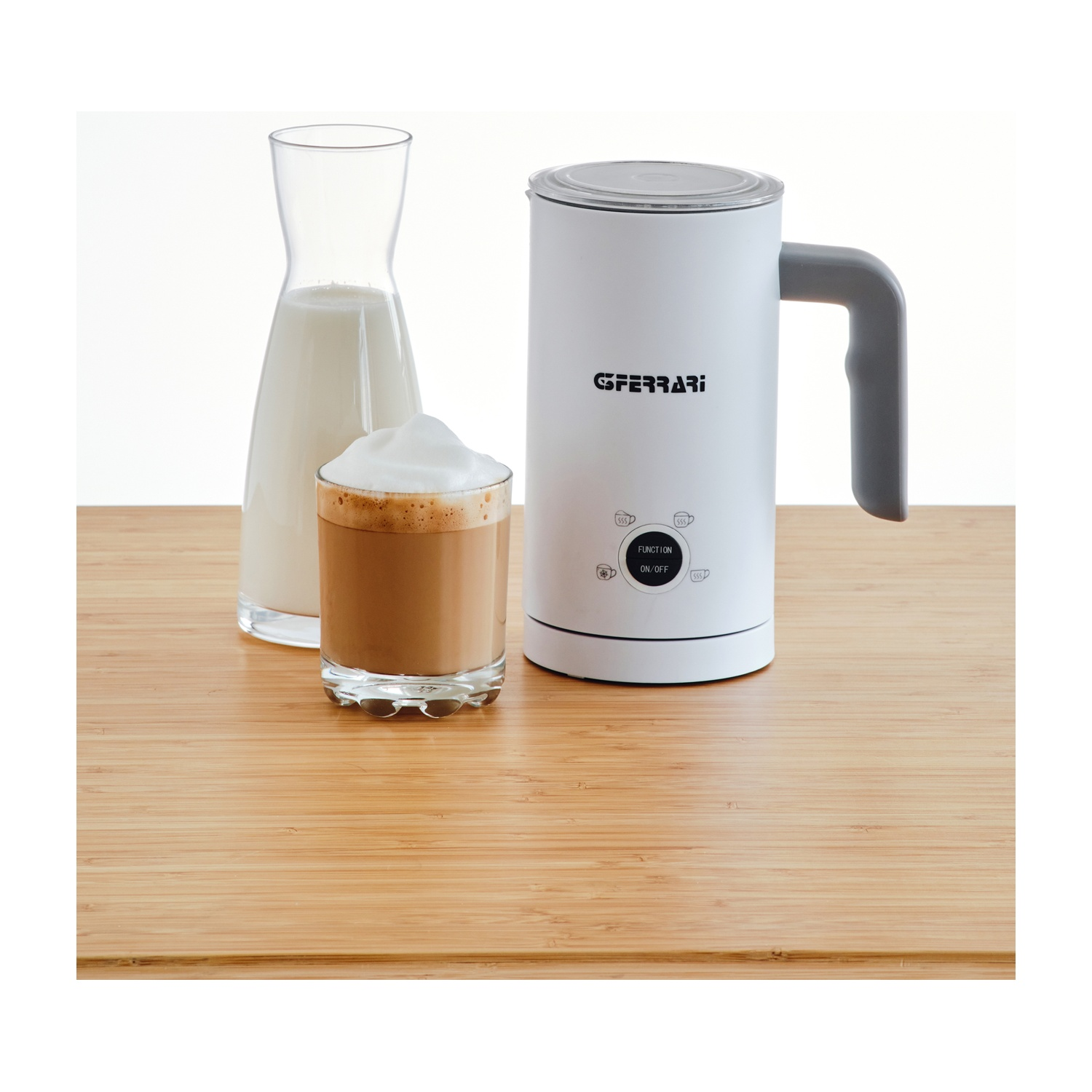 Montalatte, latte in una caraffa e un bicchiere di caffè schiumato su una superficie di legno.