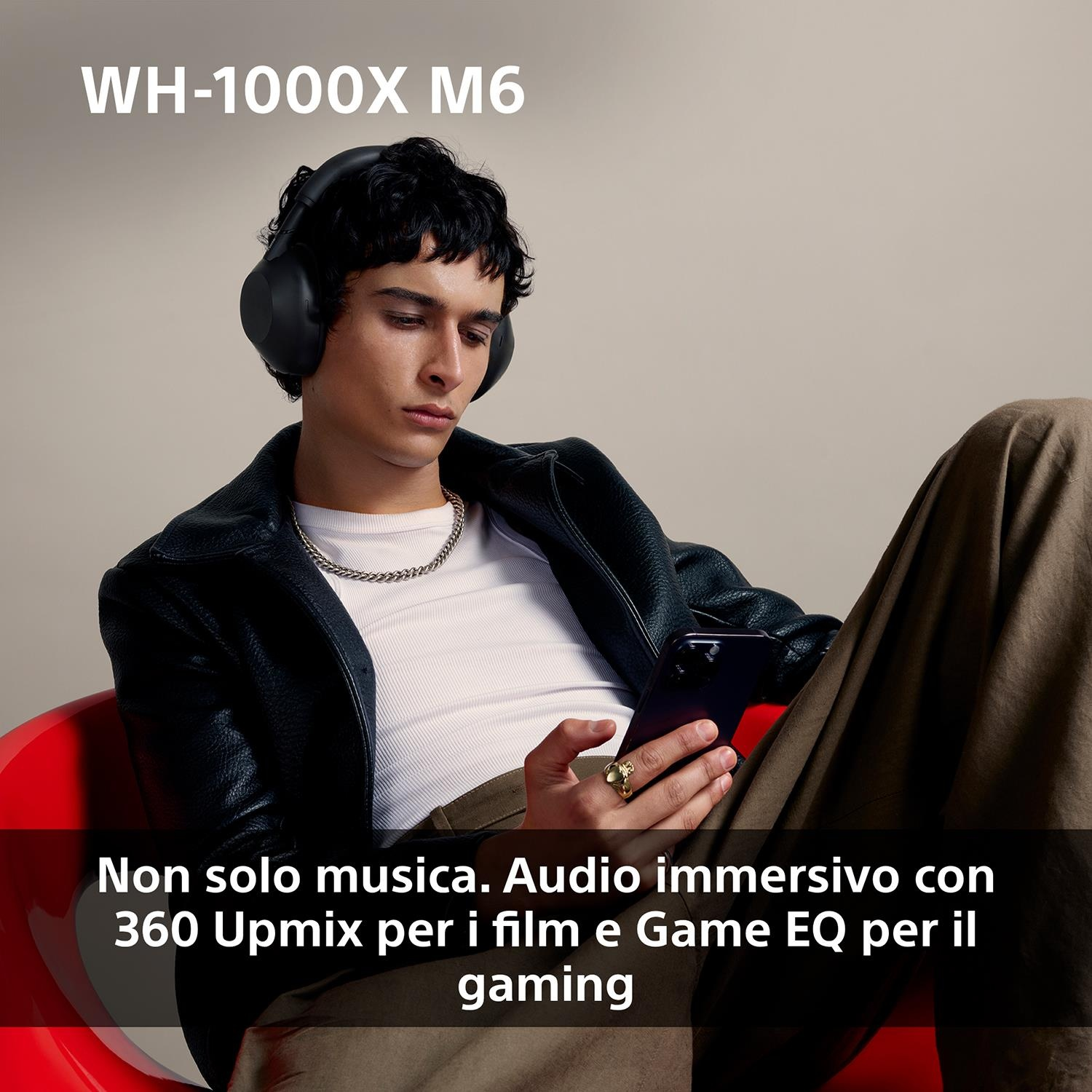 Uomo con cuffie nere, che tiene un telefono, seduto su una sedia rossa.