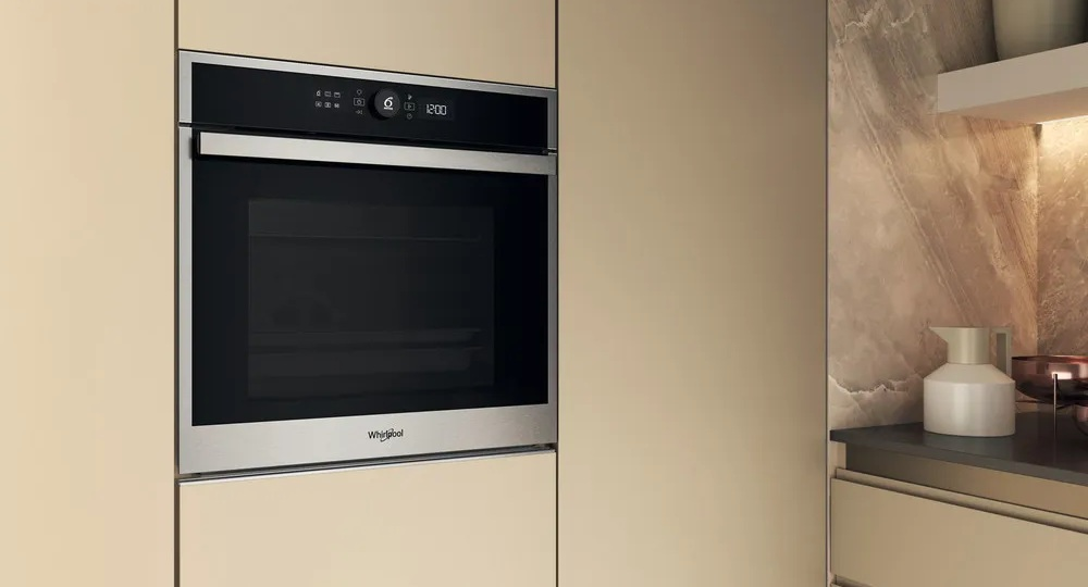 Piekarnik wbudowany w beżową szafkę kuchenną. Piekarnik ma wyświetlacz z godziną 12:00.