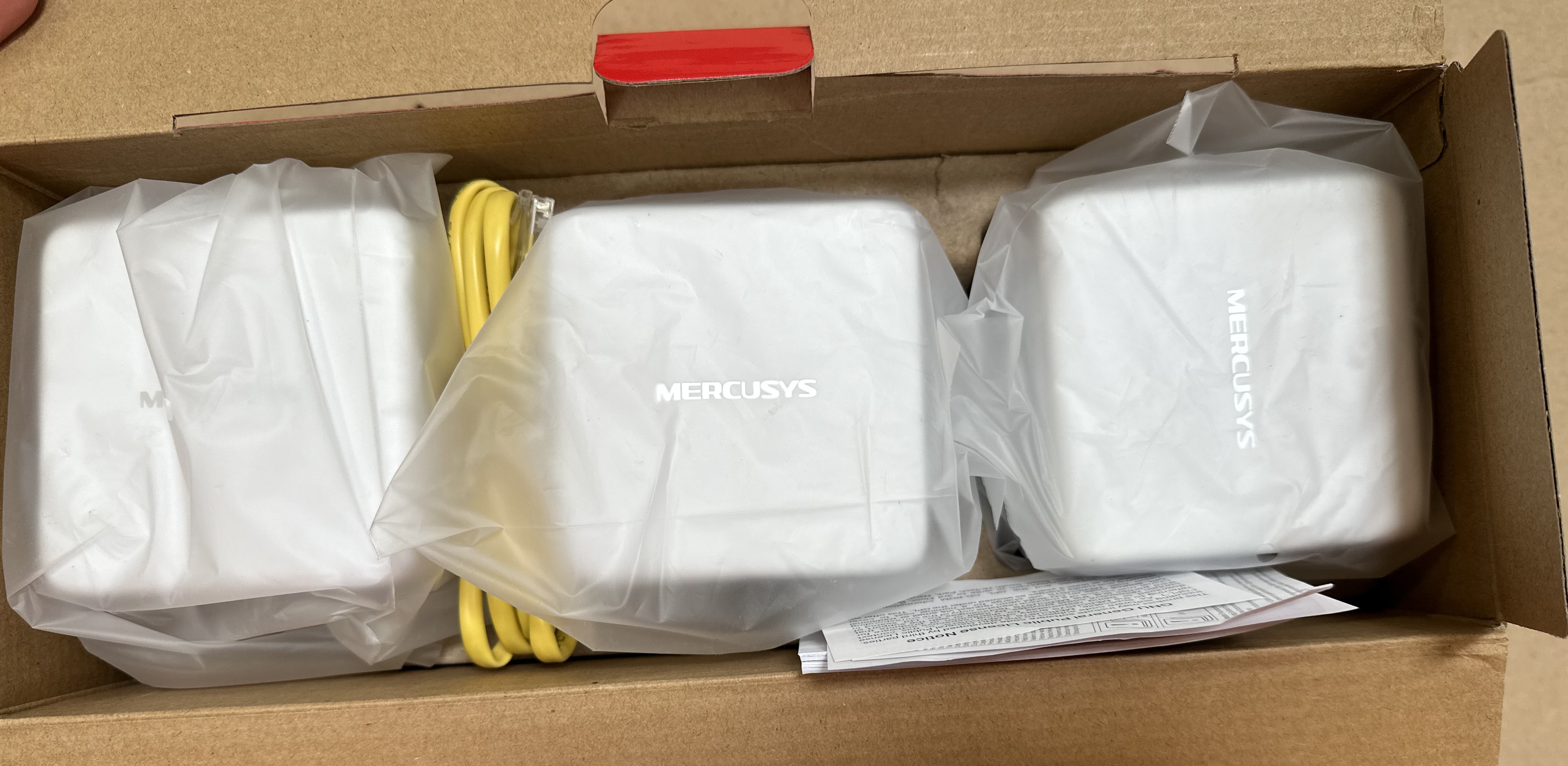 Wewnątrz pudełka Mercusys: trzy jednostki Wi-Fi mesh, żółty kabel i instrukcje.