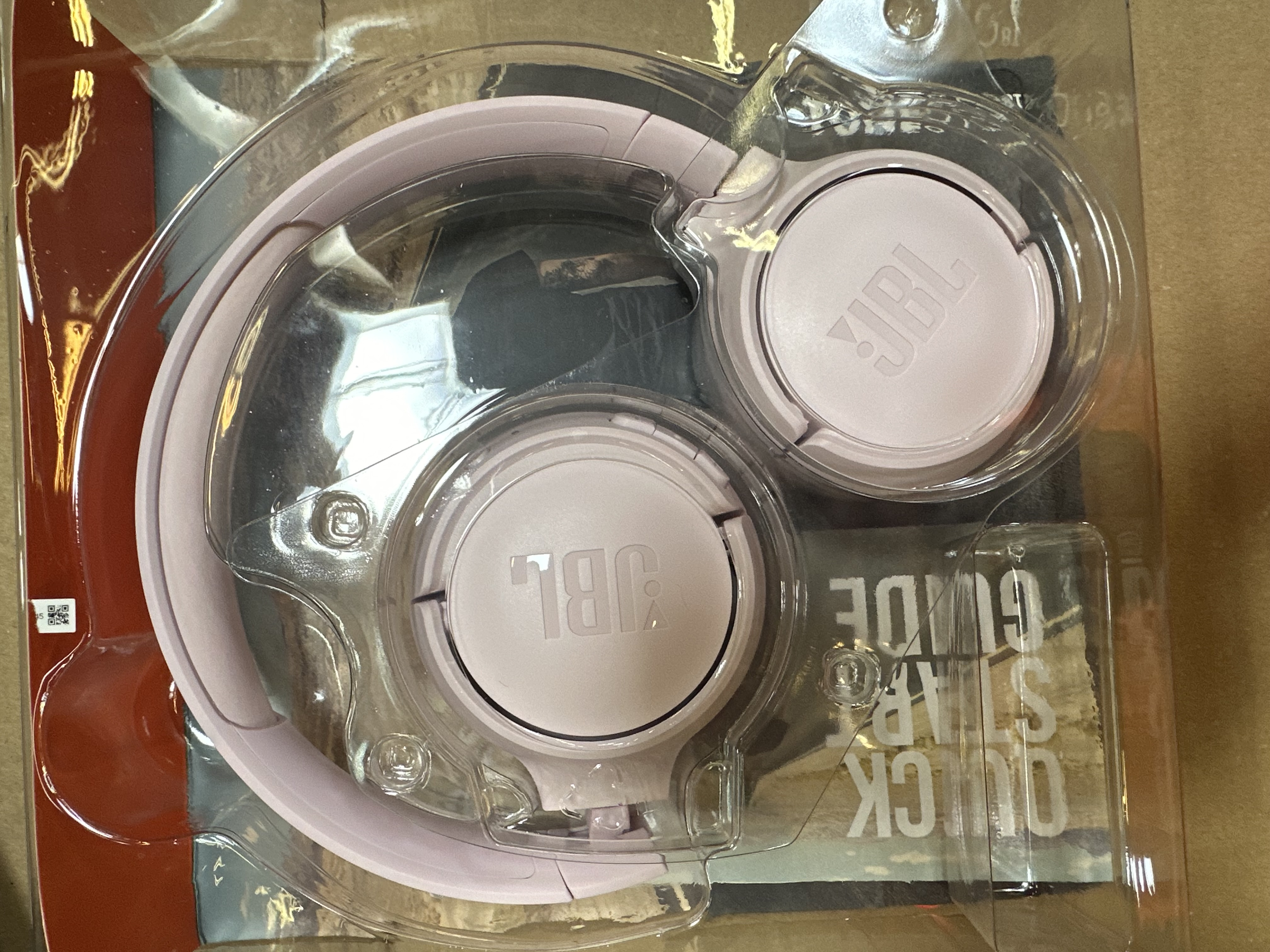 Różowe słuchawki JBL w plastikowym opakowaniu. Dołączona jest instrukcja szybkiego startu.