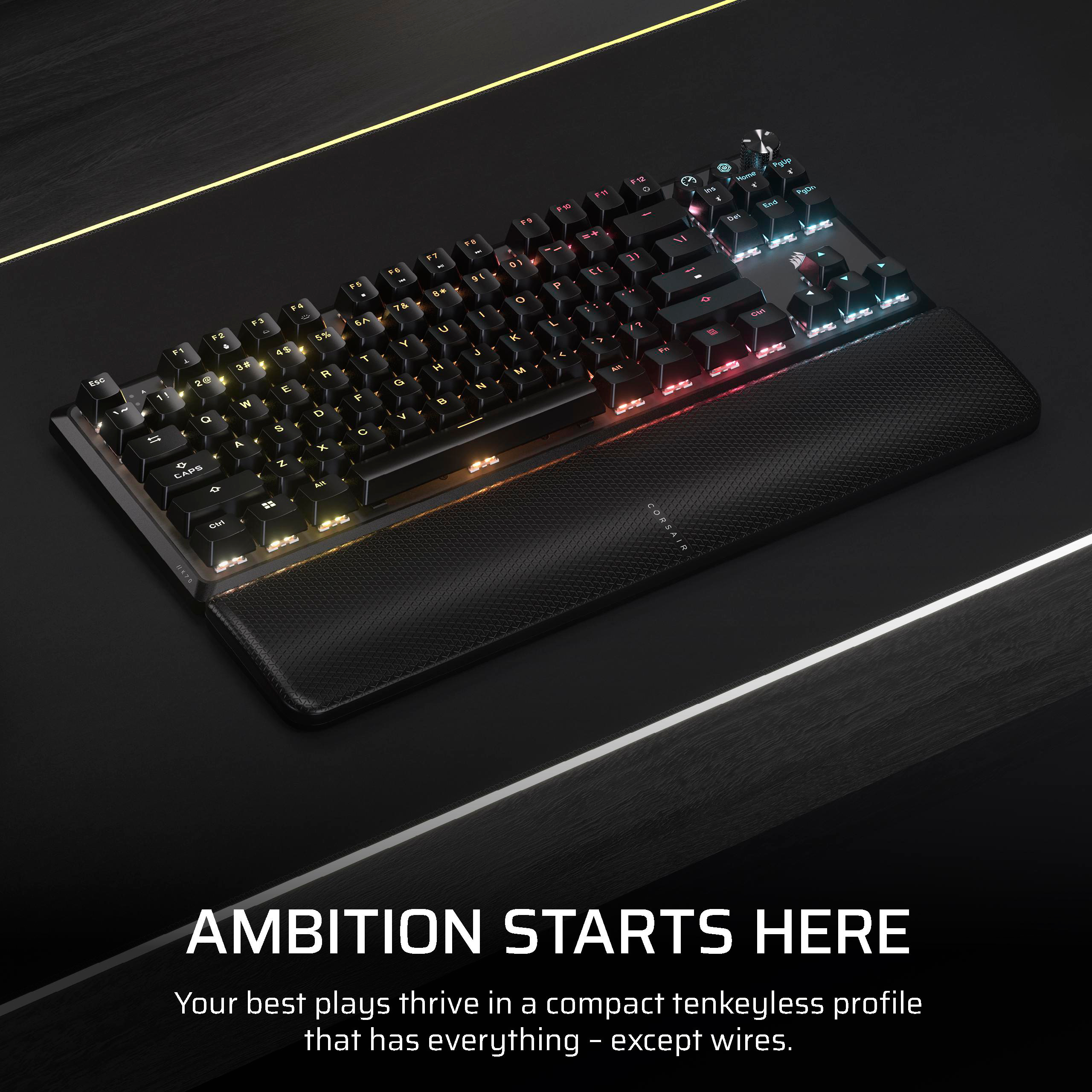 Schwarze Tastatur mit RGB-Beleuchtung, Handballenauflage auf dunkler Oberfläche. Text lautet 'Ambition Starts Here'.