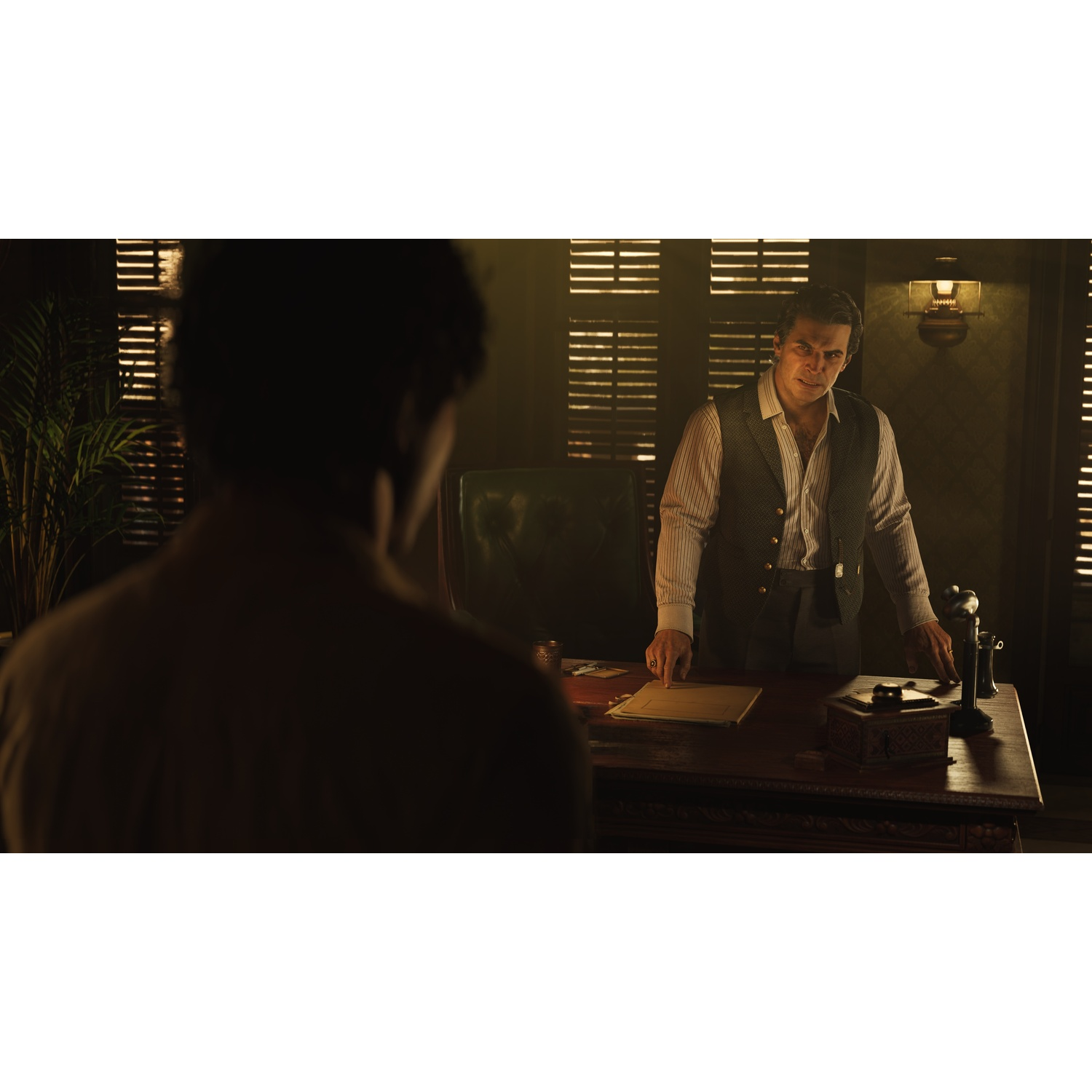 Man in office talking to another man, with a desk and blinds.