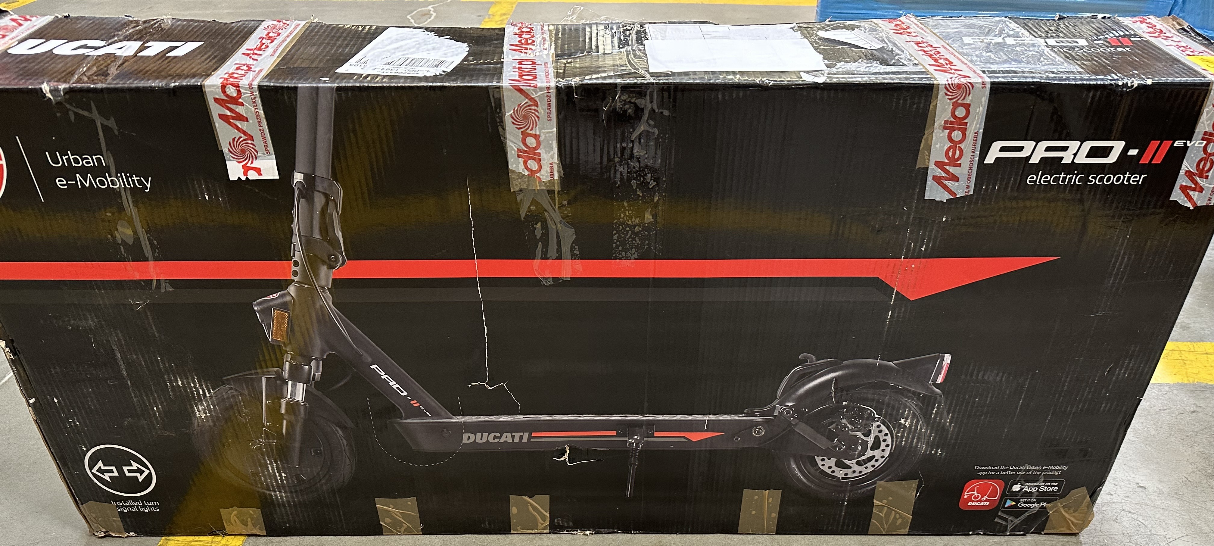 Hulajnoga elektryczna Ducati PRO-II w pudełku. Czarna hulajnoga z czerwonymi akcentami. Widoczny tekst.