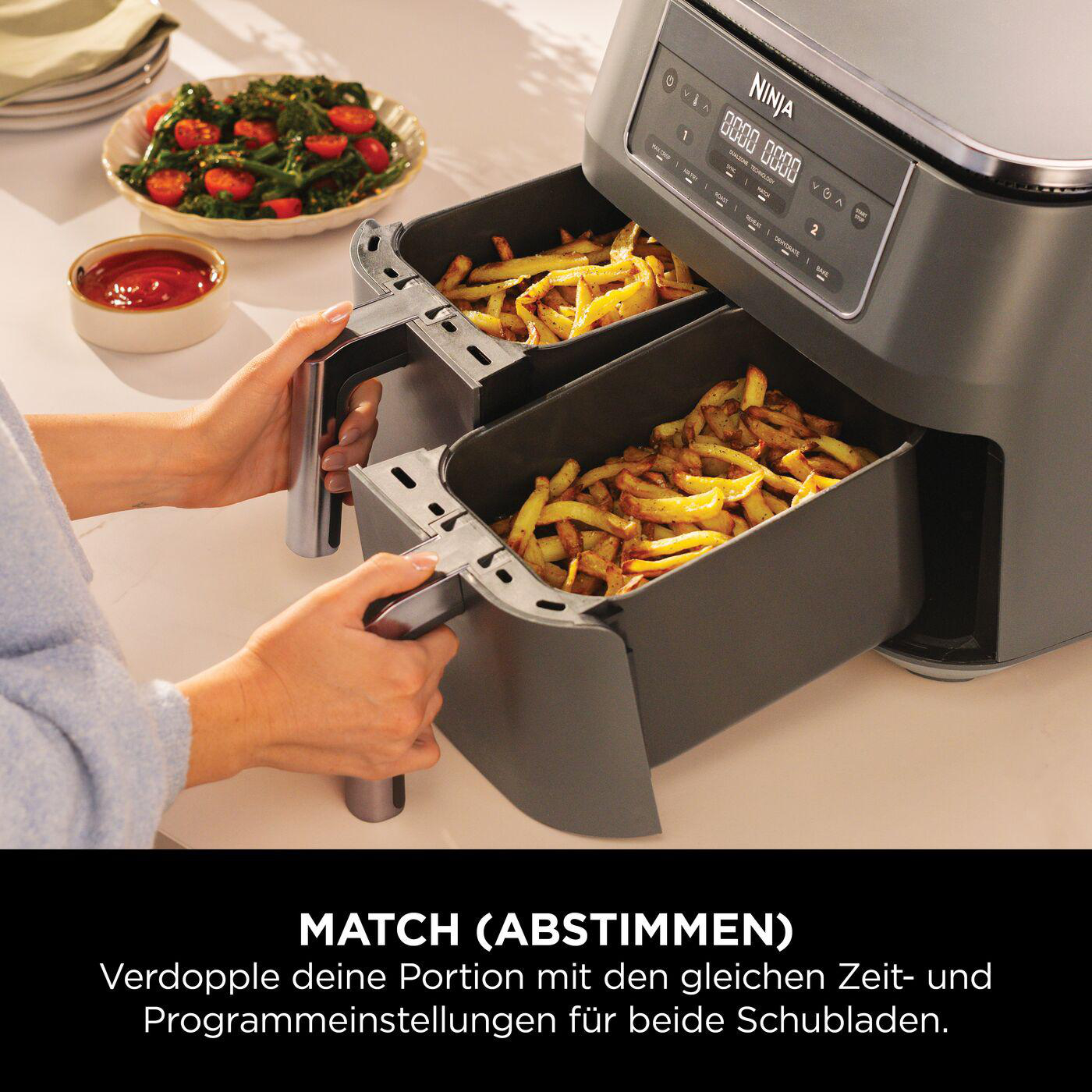 Ninja Heißluftfritteuse mit Essen. Zwei Körbe mit Pommes. Hände halten die Körbe.