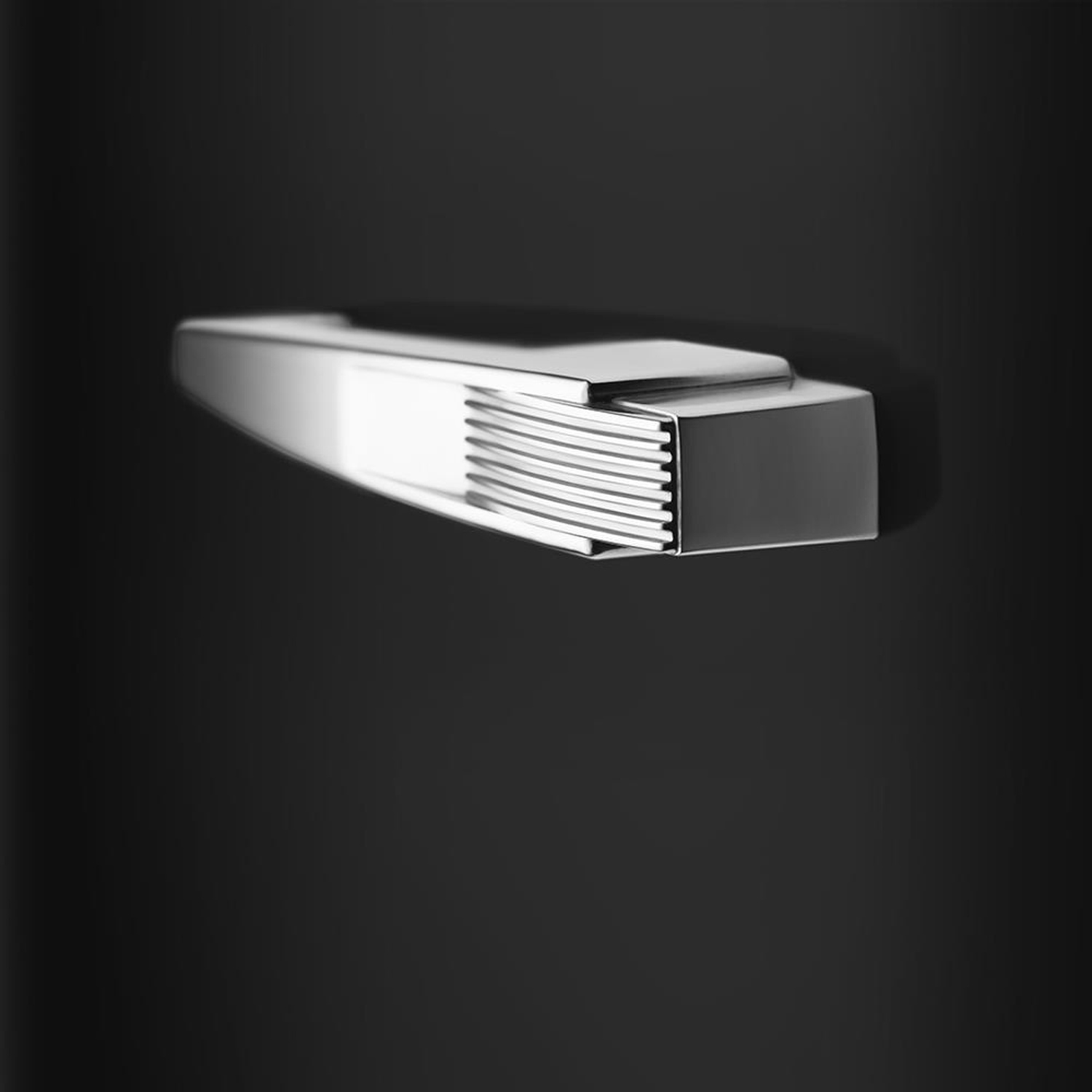 Primo piano di una maniglia del frigorifero argentata su una superficie nera. La maniglia ha un design elegante.