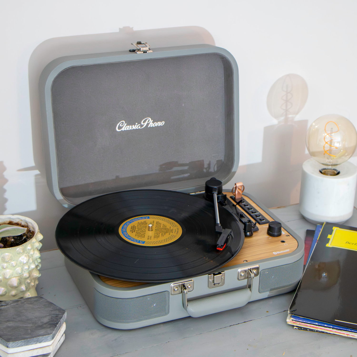 Open gray Classic Phono turntable with record spinning.  Light bulb and coasters on the side.