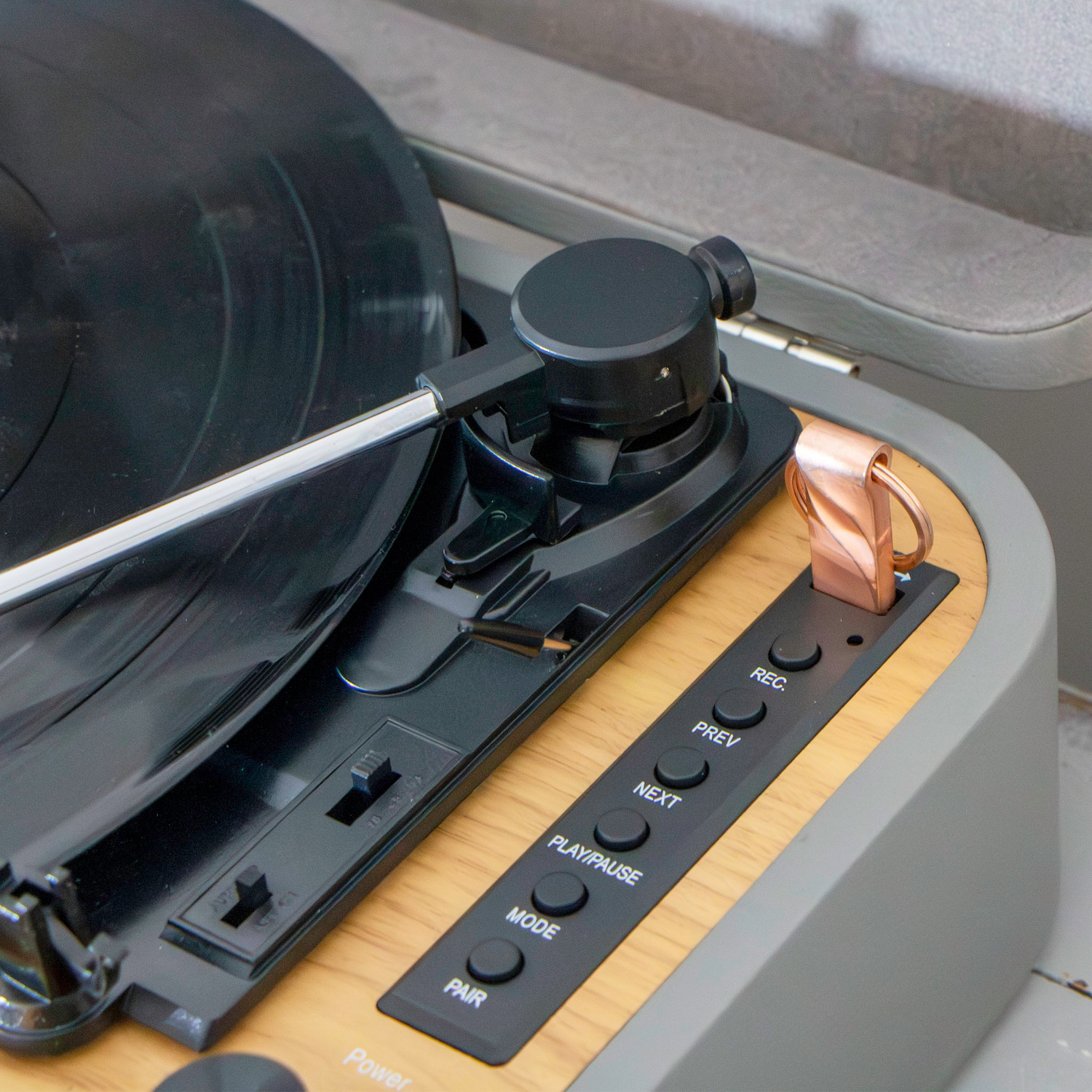 Close-up of turntable controls. Black arm, wooden panel with buttons and knobs.