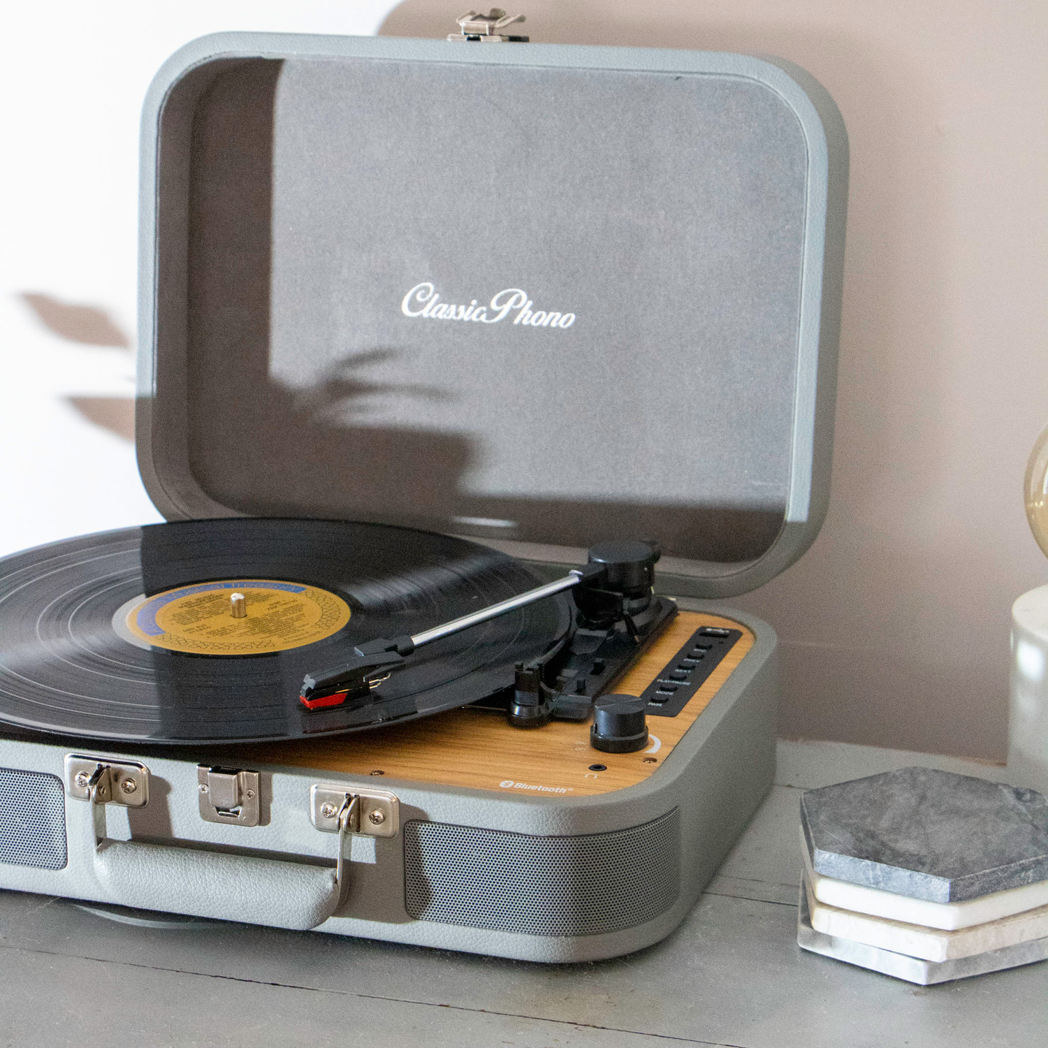 Open gray Classic Phono turntable. Record spinning. Wooden panel with buttons and knobs.