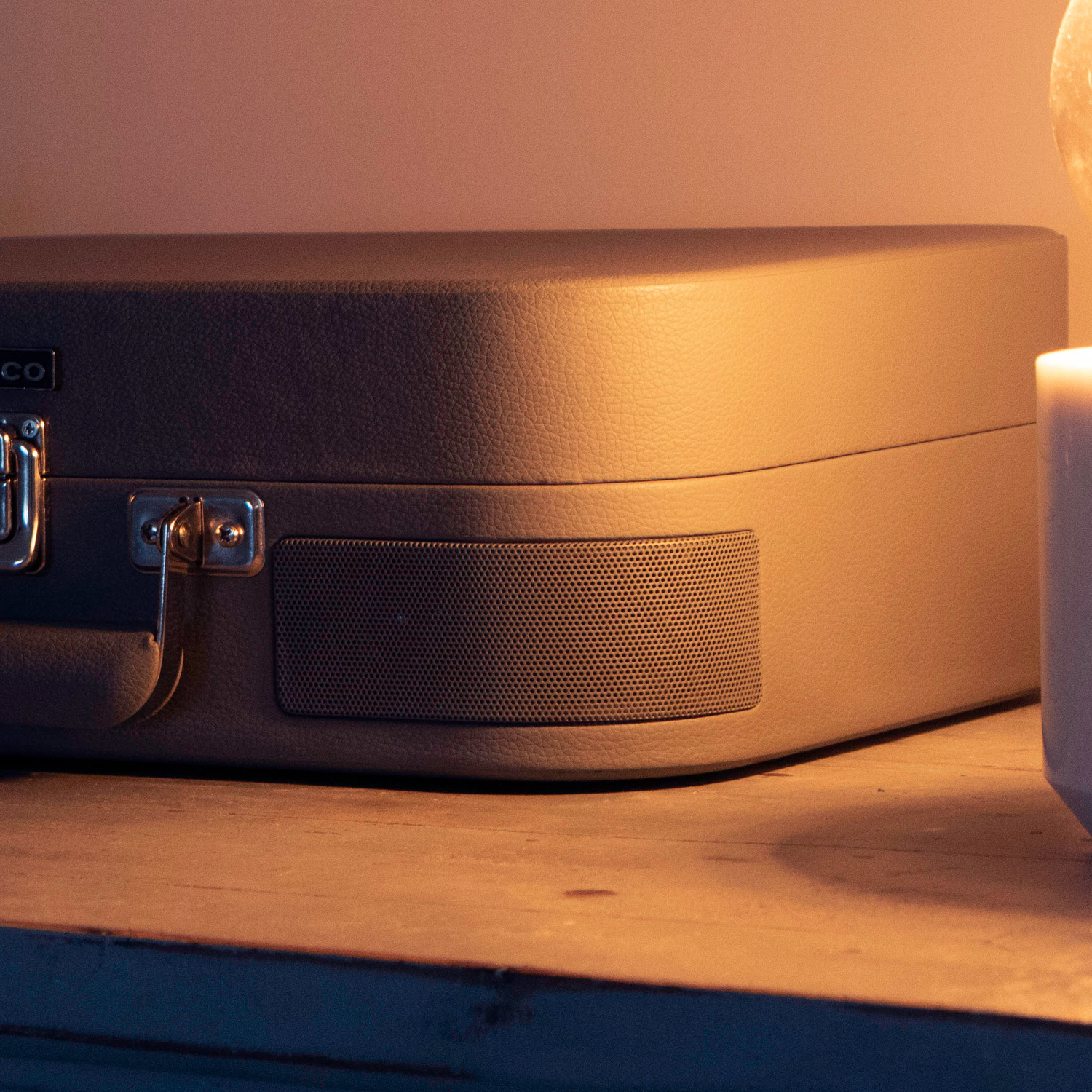 A grey Lenco record player in a closed suitcase shape, on a wooden table, lit by warm, dim light.