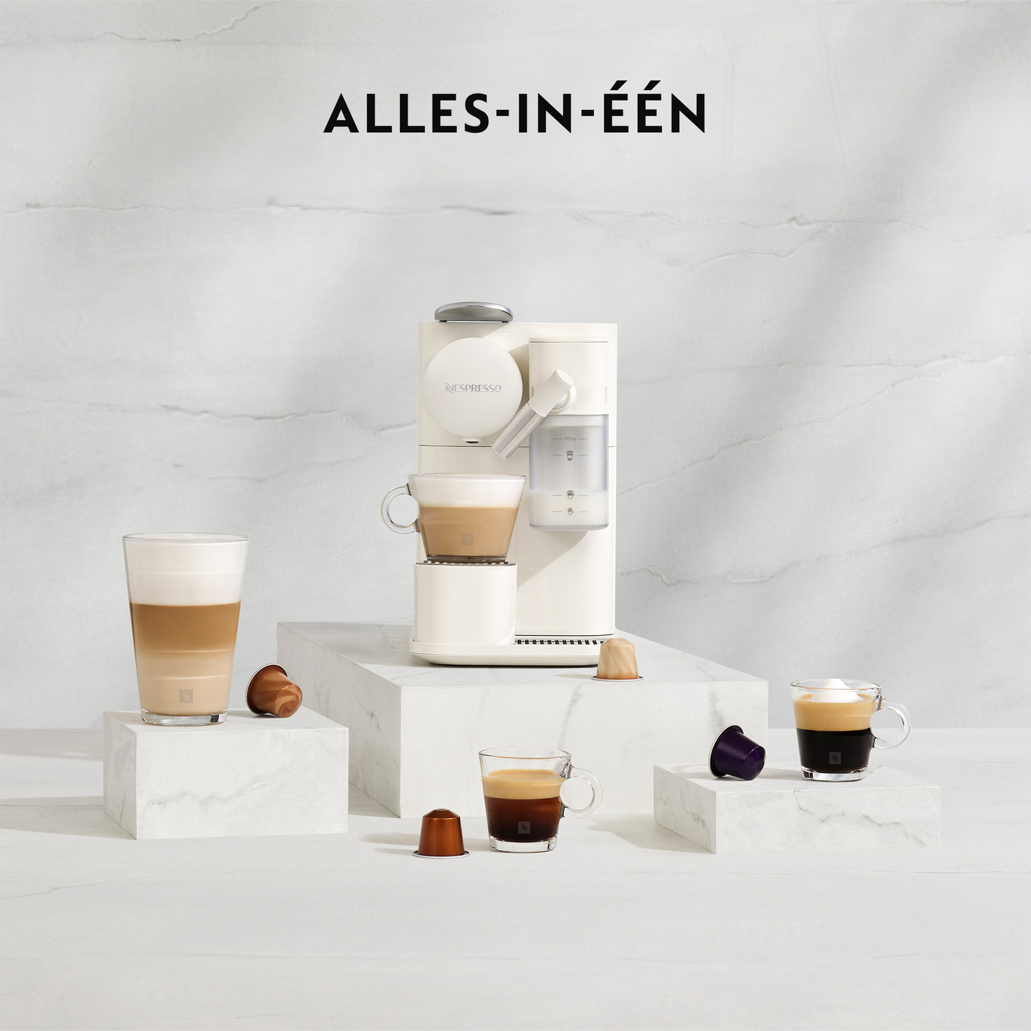 Een witte koffiemachine met verschillende kopjes op een marmeren oppervlak. Koffiecapsules verspreid.