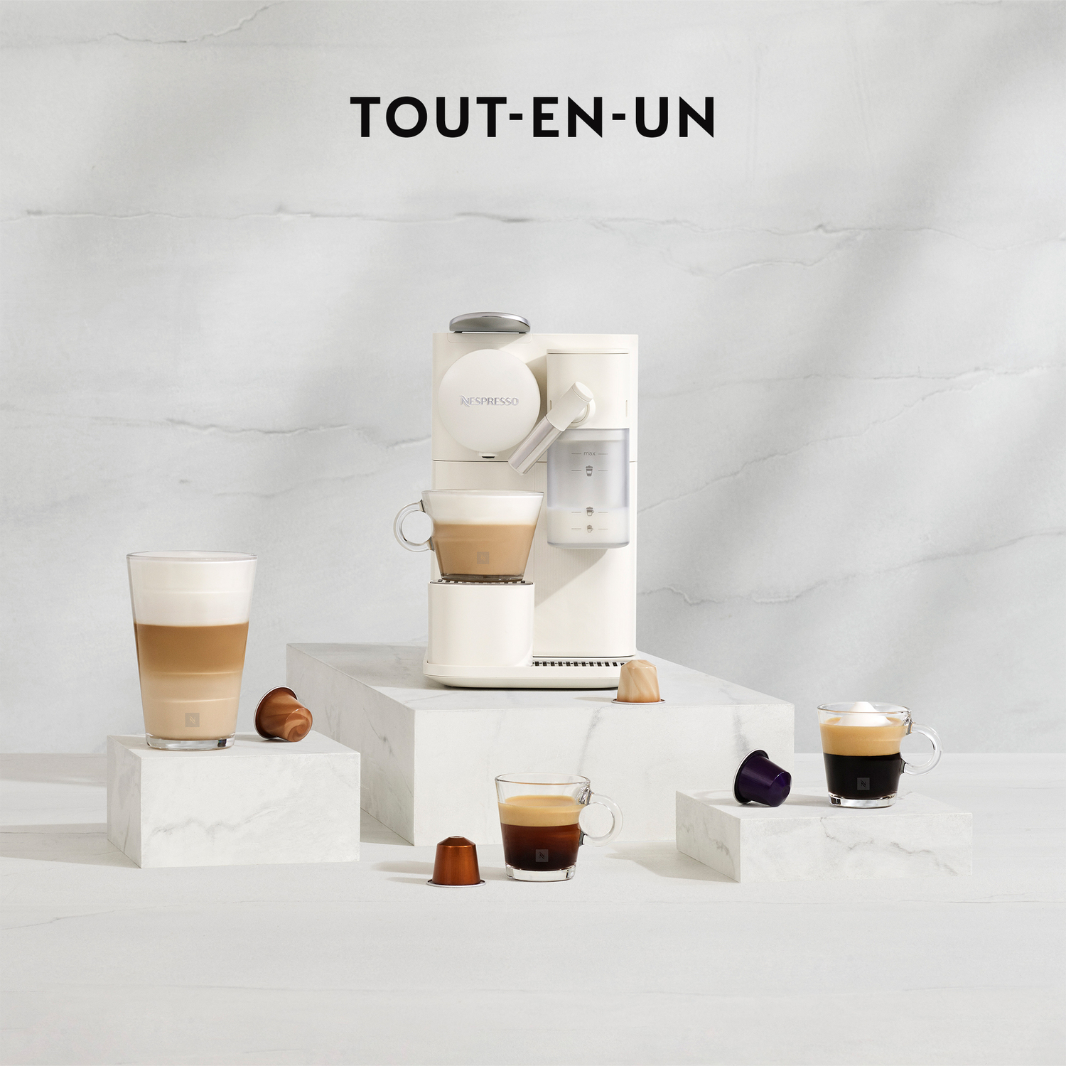 Une machine à café blanche avec une sélection de tasses sur une surface en marbre, avec des capsules dispersées.