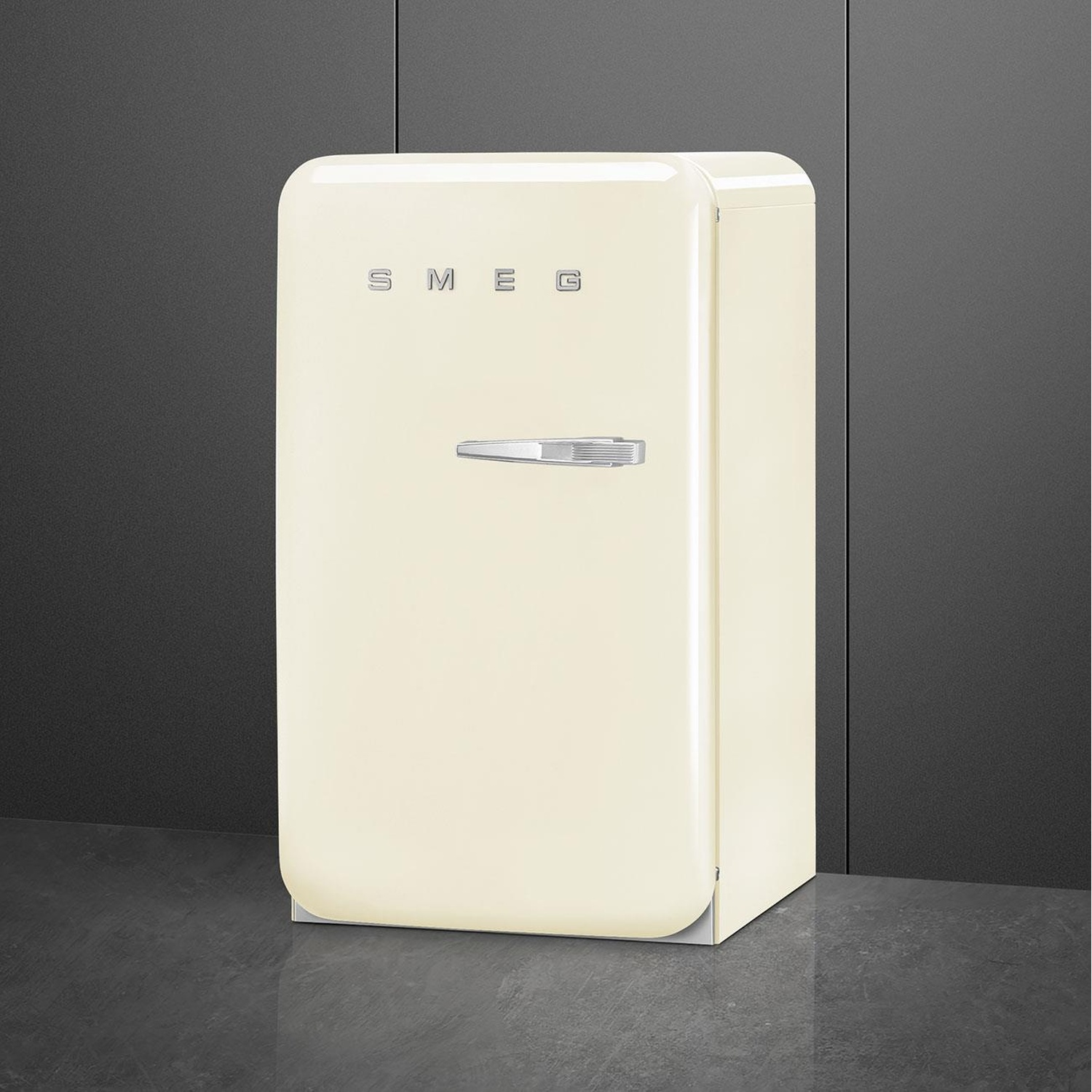 Frigorifero Smeg crema. Maniglia argento, logo SMEG. Sfondo e pavimento grigio scuro. Vista angolata.