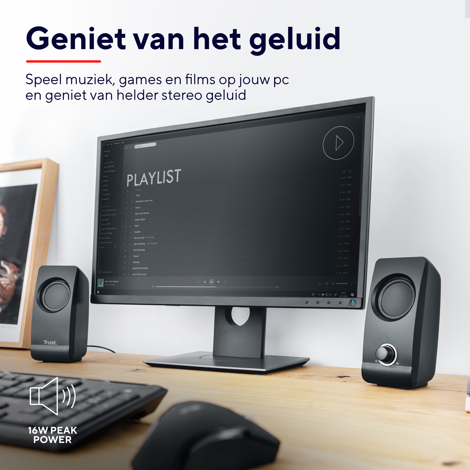 Black speakers on a wooden desk with a computer monitor displaying a playlist.