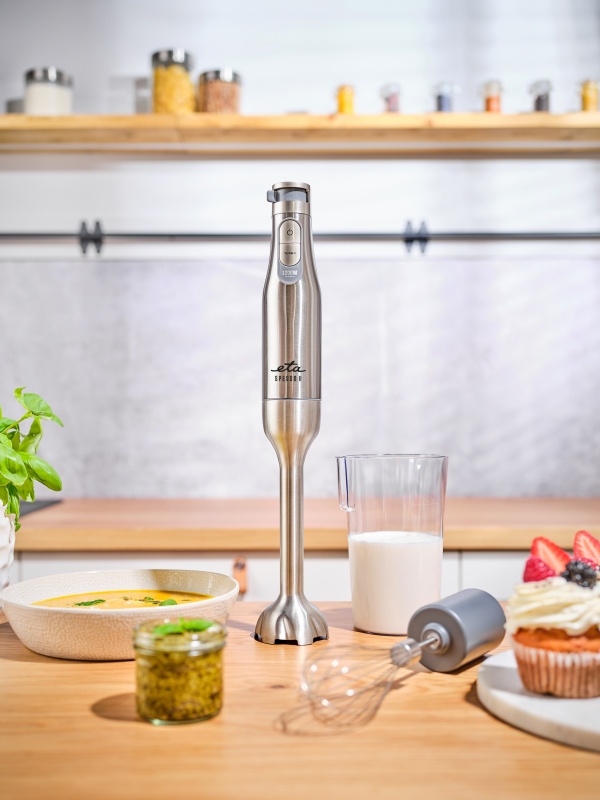 Kézi mixer egy fa asztalon. Egy csésze tej, pesto és tejszínhab.