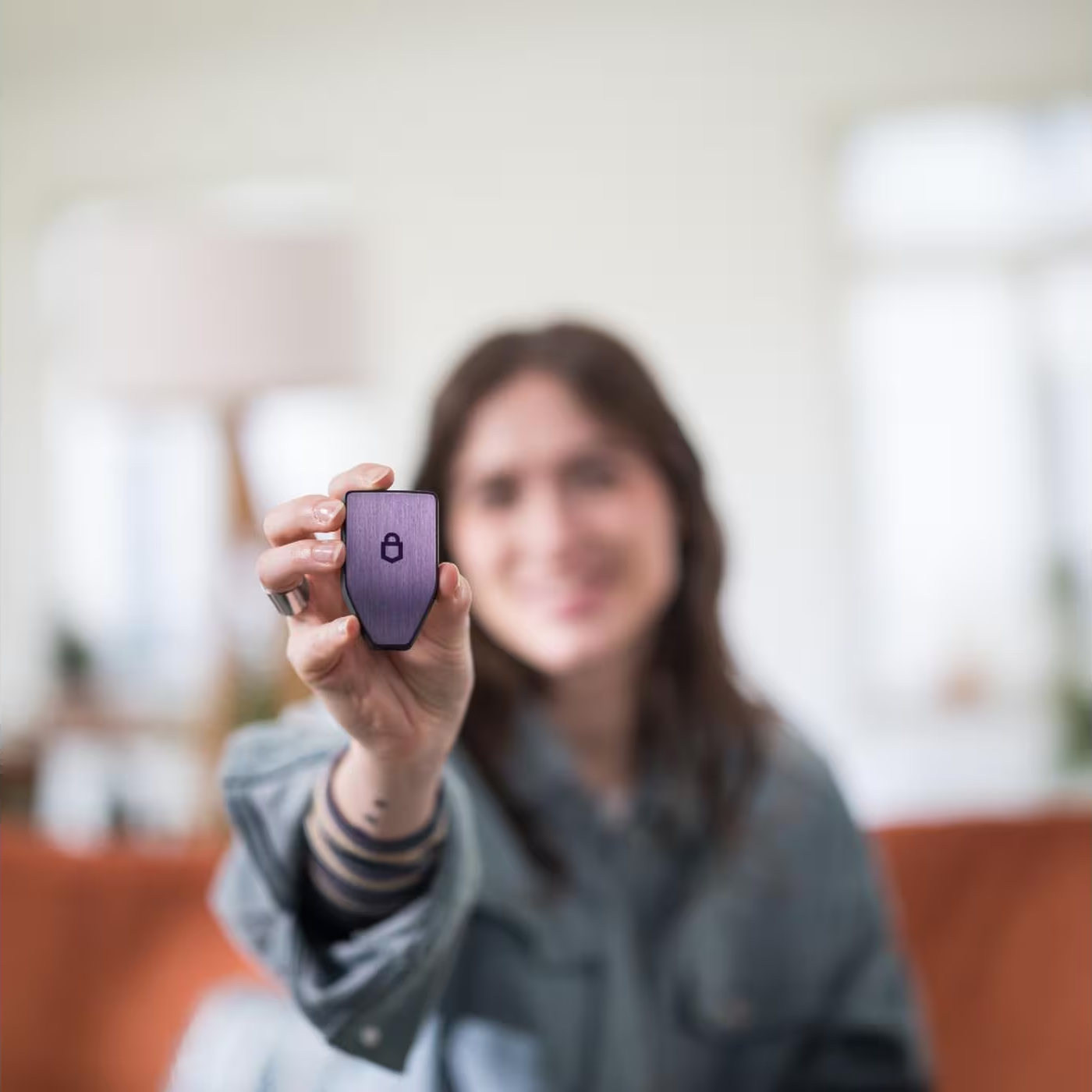 Femme tenant un appareil numérique noir avec une icône de cadenas. L'appareil est un Trezor Safe 5.