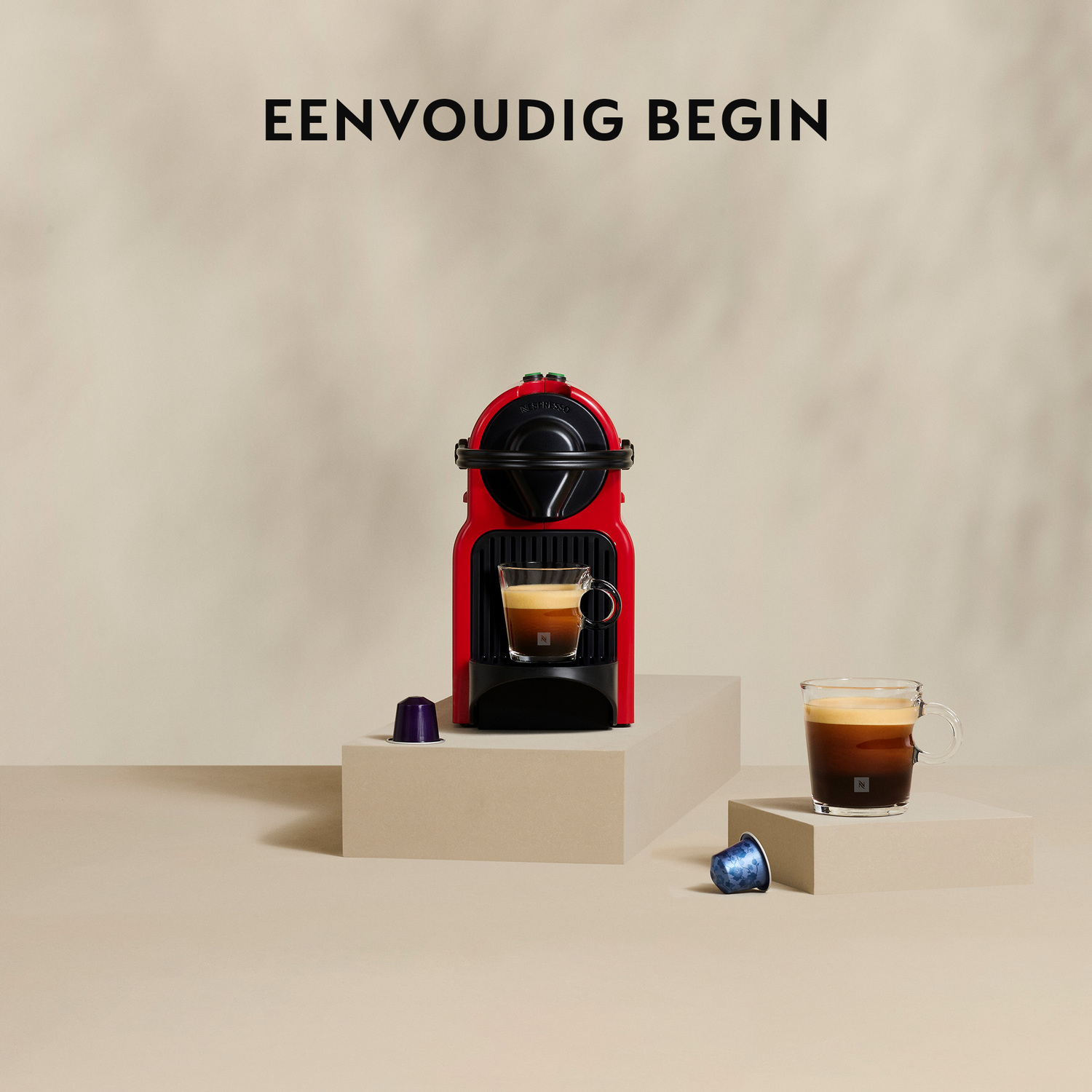 Red coffee machine with a cup of coffee. Two capsules are on the floor. Text says 'Eenvoudig Begin'.
