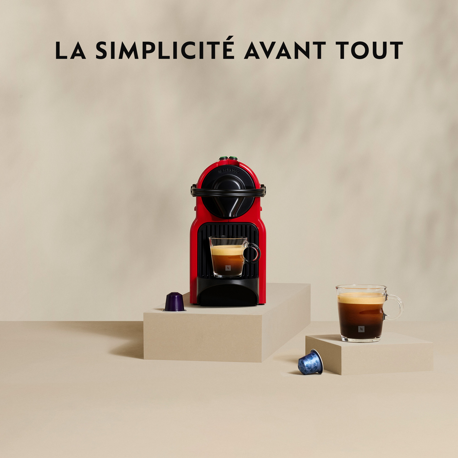 Machine à café rouge avec une tasse de café. Deux capsules sont au sol. Le texte dit 'La Simplicité Avant Tout'.